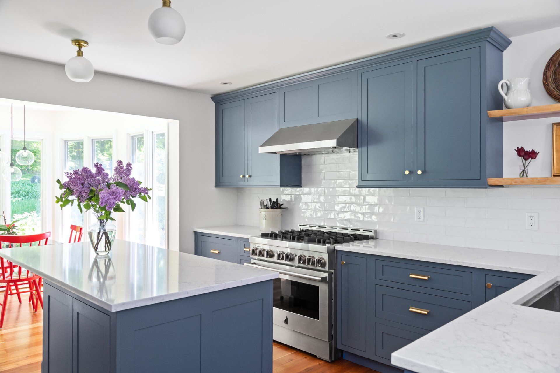 Bright modern kitchen with blue cabinets, white countertops, stainless stove, and a vase of purple flowers on the island