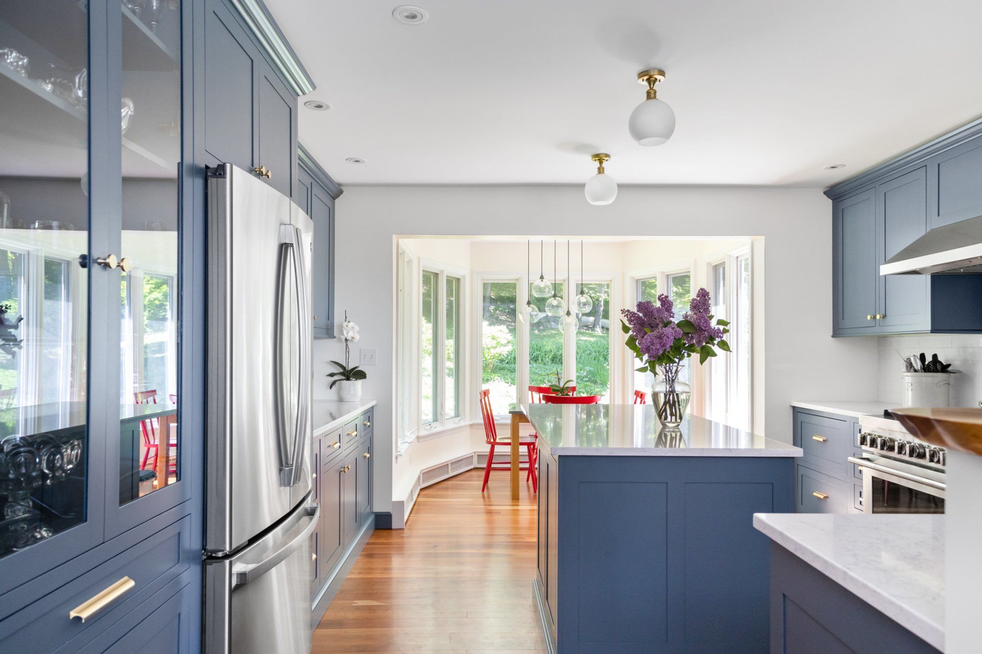 Bright blue kitchen with stainless fridge, white counters, and a dining nook by sunlit windows