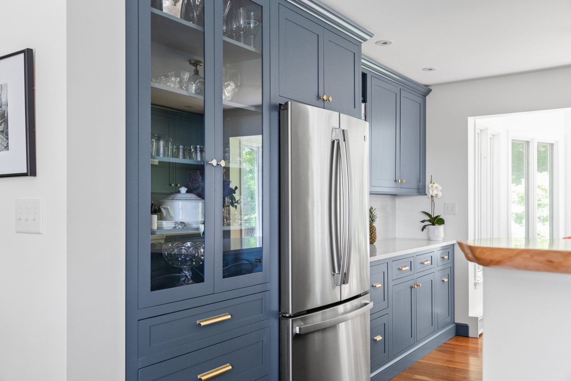 Bright blue kitchen with stainless steel fridge, glass-front cabinets, and a sunlit dining nook.