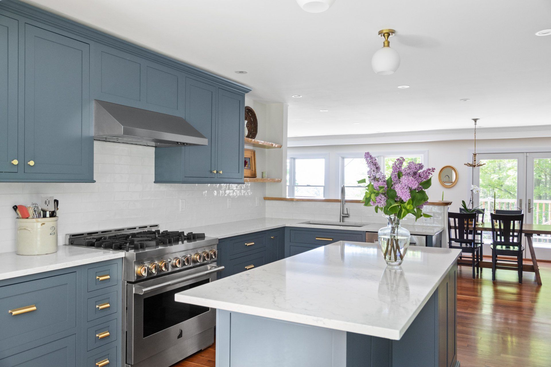 Bright blue kitchen with white island, stainless stove, and dining area beyond a windowed opening
