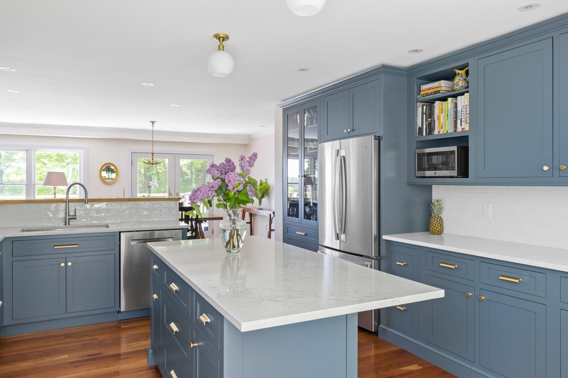 Bright blue kitchen with white island, stainless fridge, and purple flowers on the counter