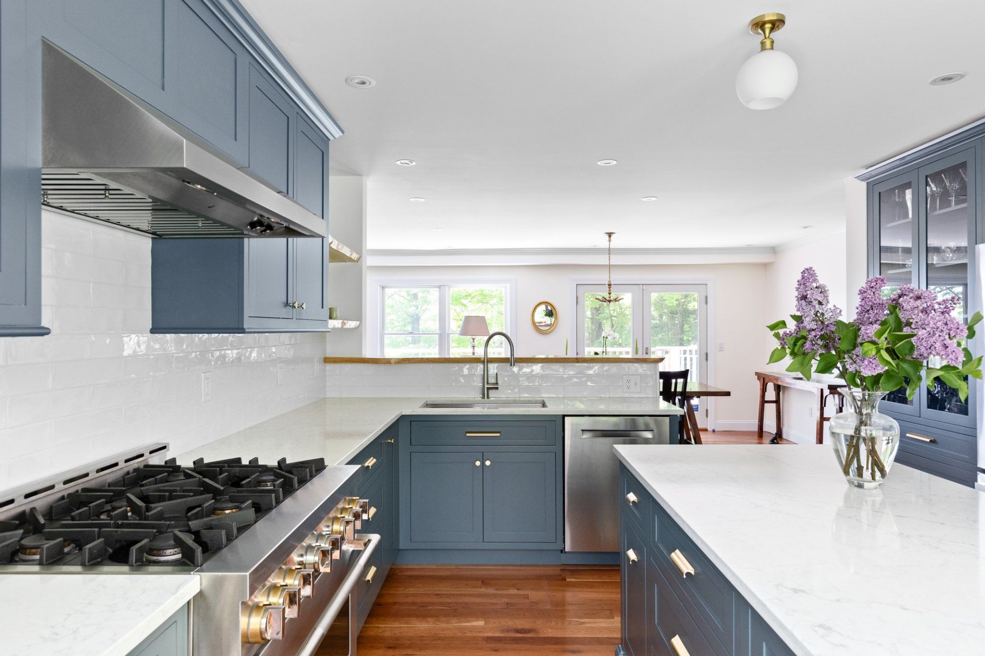 Bright modern kitchen with blue cabinets, white countertops, gas stove, and a vase of purple flowers.