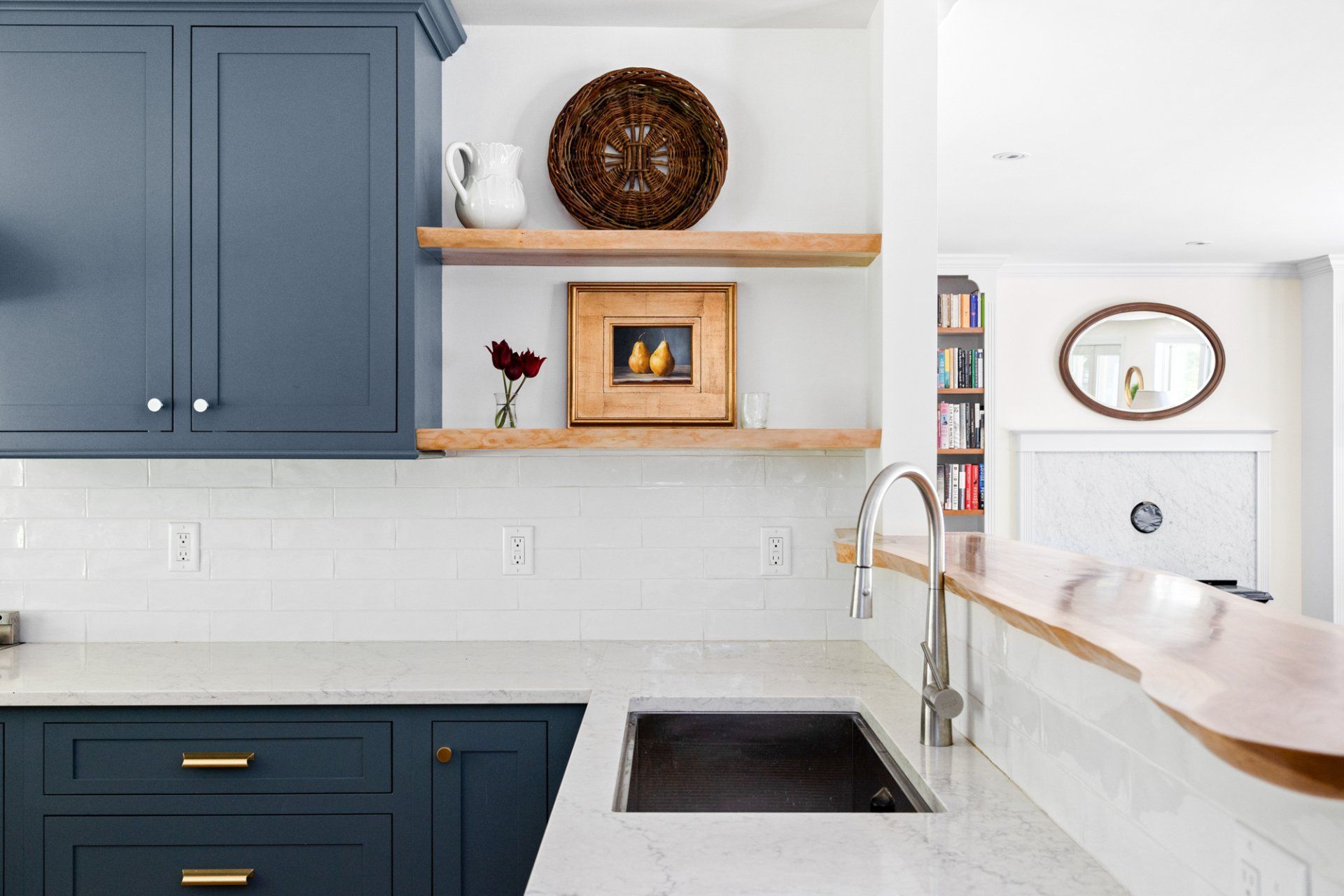 Modern kitchen with navy cabinets, white countertops, wood shelves, and a sink by a bright window