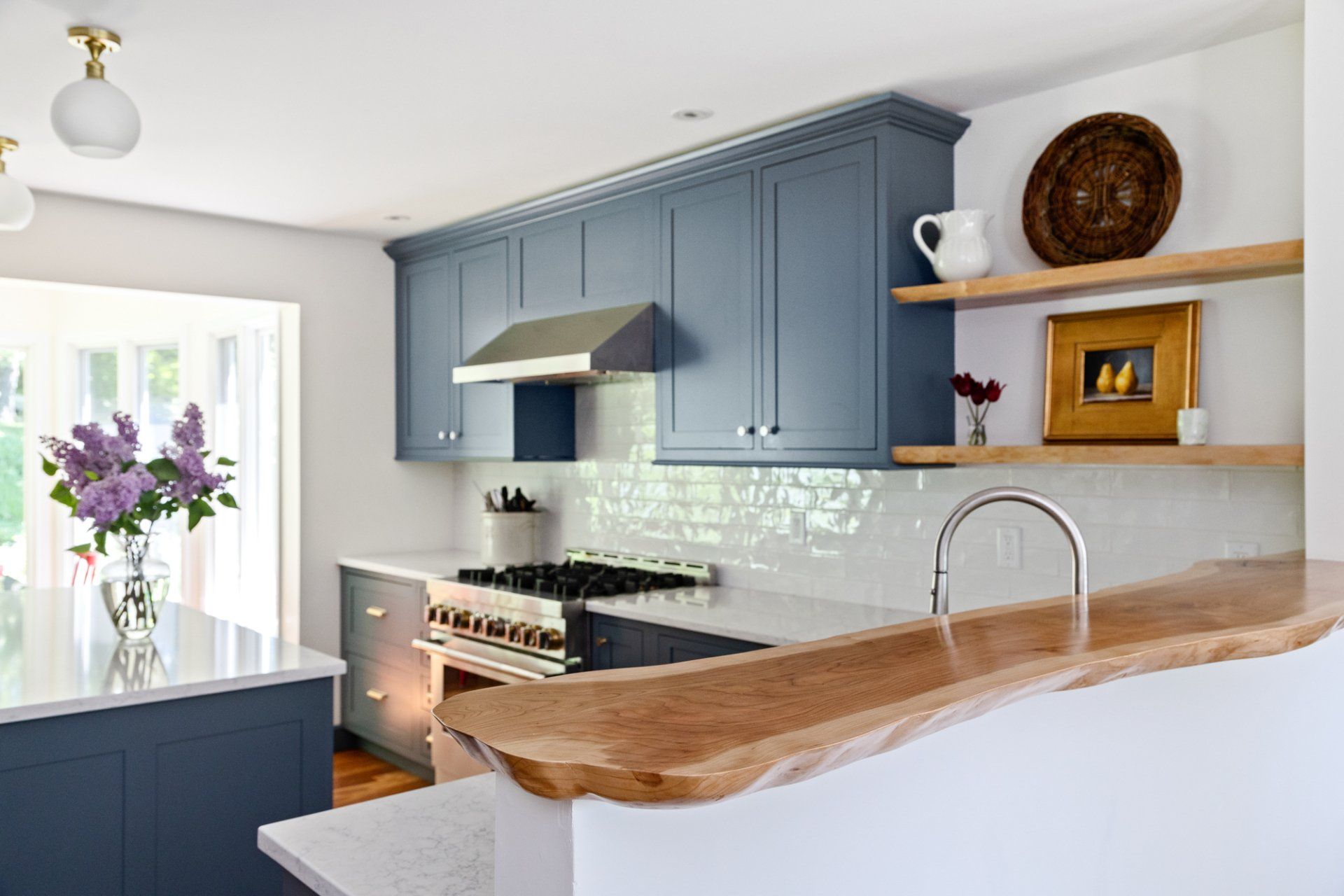 Bright kitchen with blue cabinets, white countertops, wooden island, and flowers by the window.