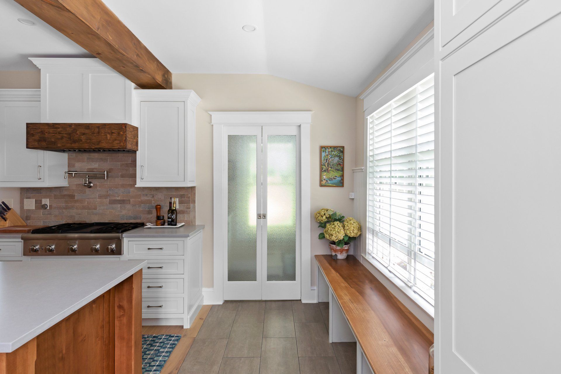 Bright kitchen with white cabinets, wood beams, glass doors, and a window bench with flowers