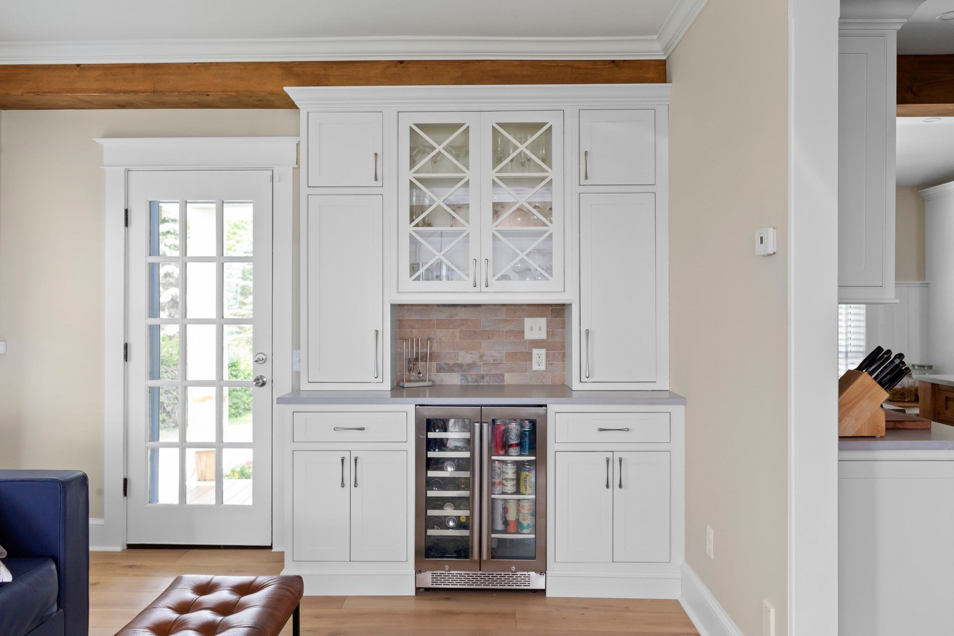 Bright white built-in wet bar with wine fridge and glass-front cabinets in a living room