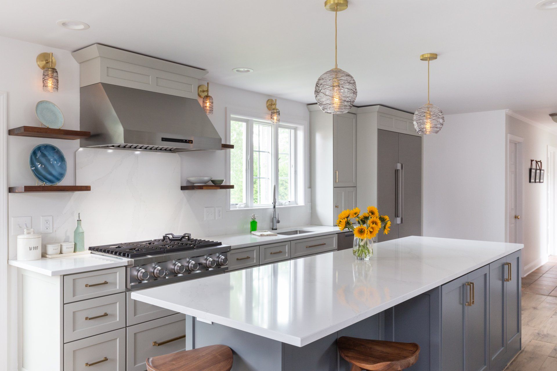 Bright modern kitchen with gray cabinets, white island, stainless range, and pendant lights