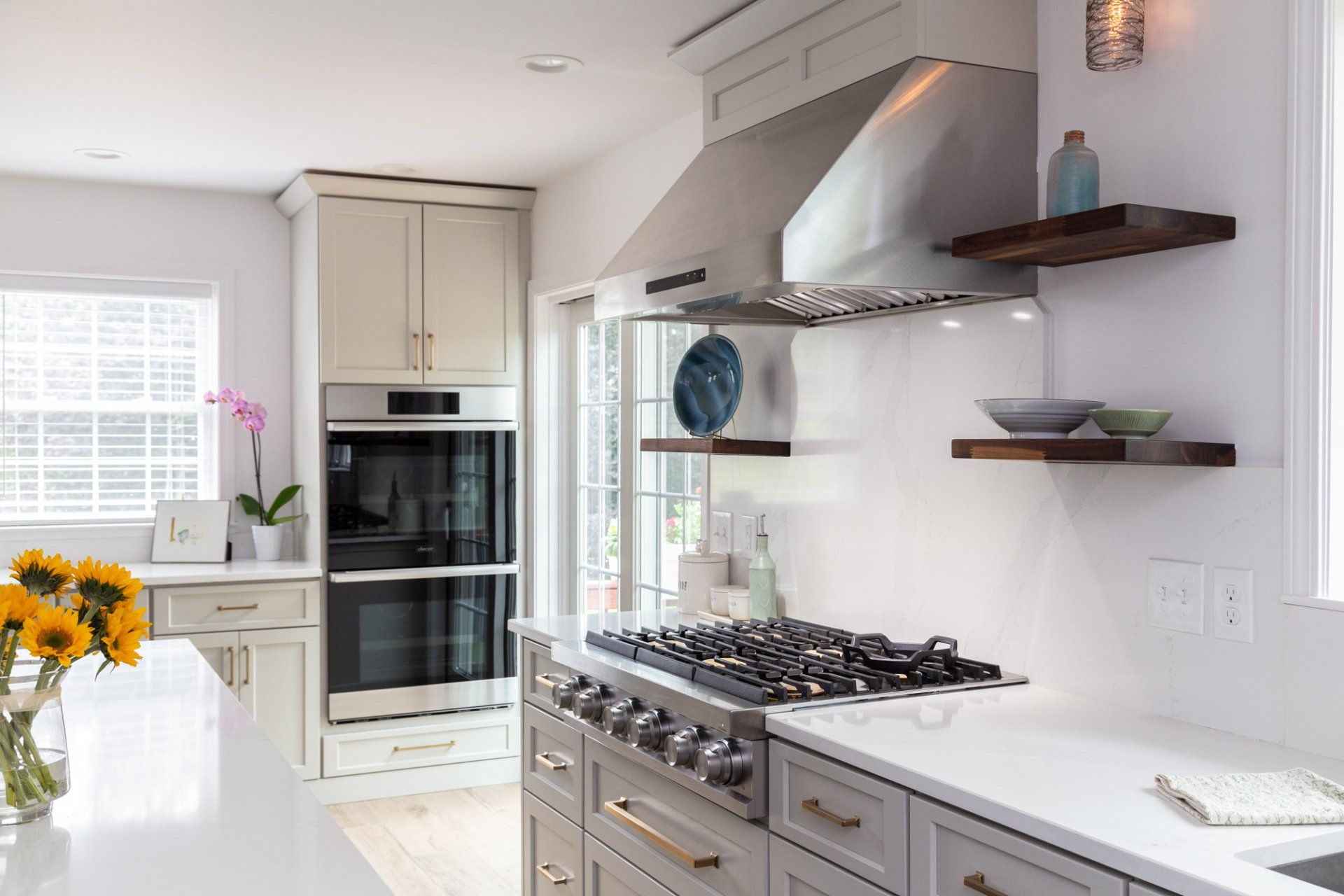 Bright modern kitchen with white cabinets, a gas range, stainless hood, and flowers on the island.