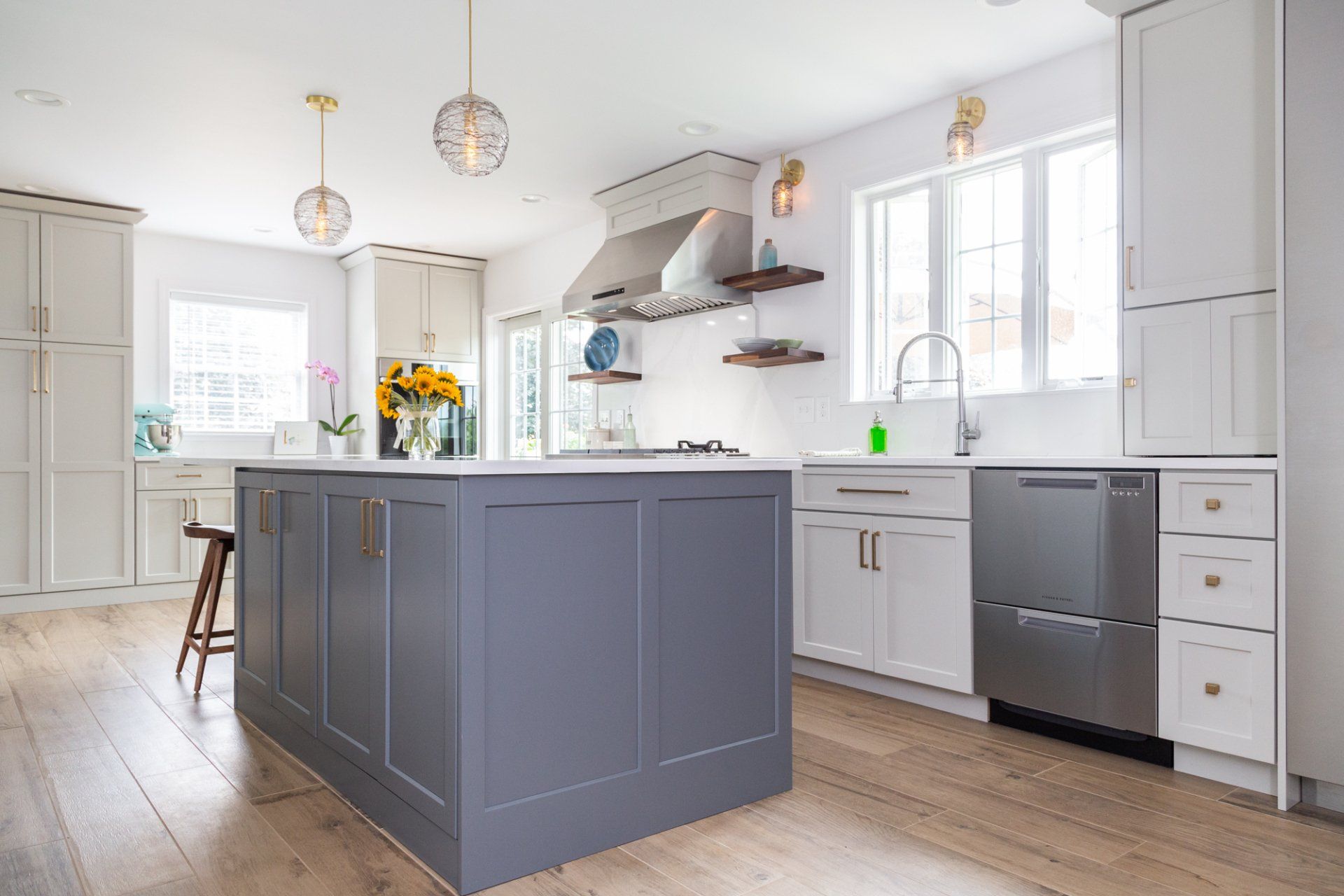 Bright modern kitchen with a gray island, white cabinets, pendant lights, and stainless steel appliances.