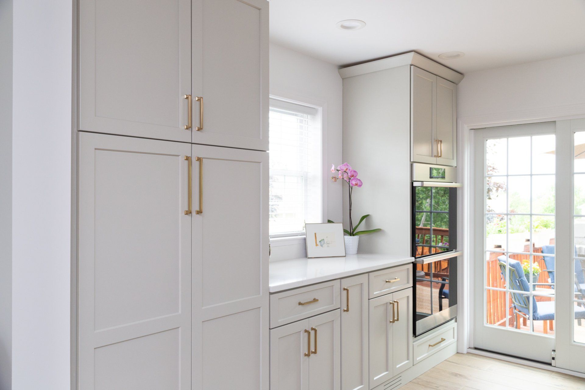 Bright white kitchen with gold handles, sink, and glass door to a patio