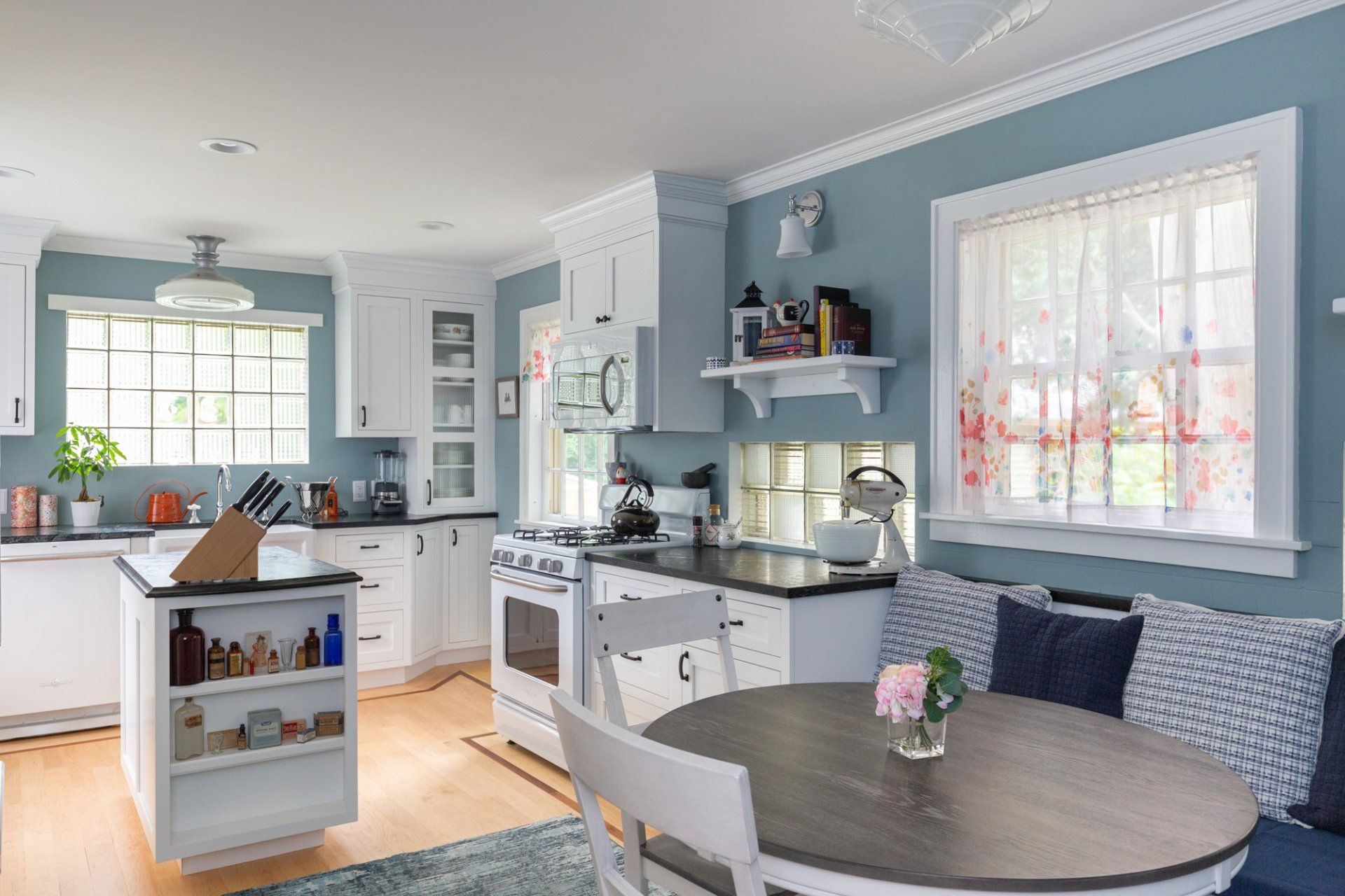 Bright blue kitchen and dining nook with white cabinets, round table, and sunlight through windows