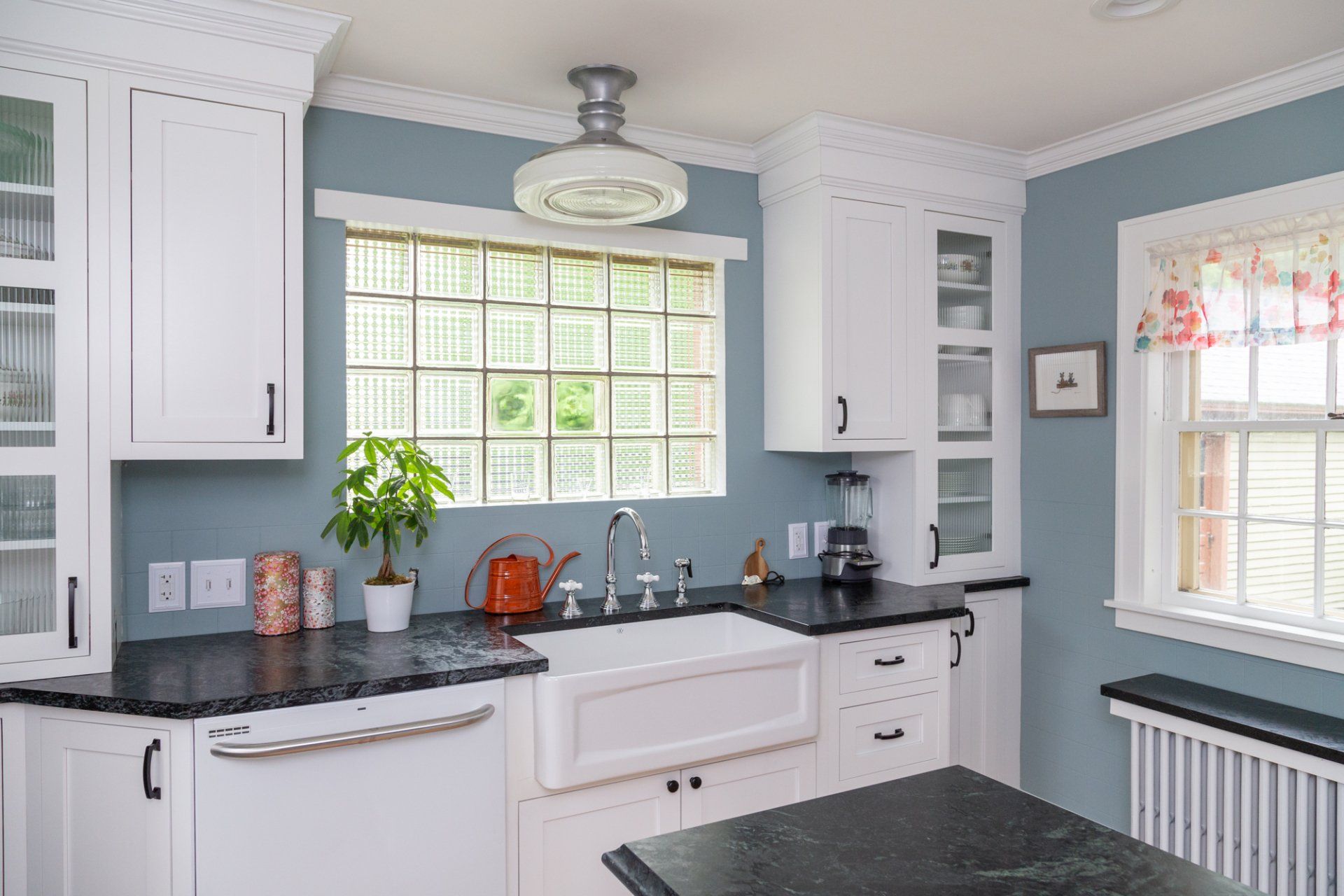 Bright white kitchen with black countertops, blue walls, and a window over the sink.