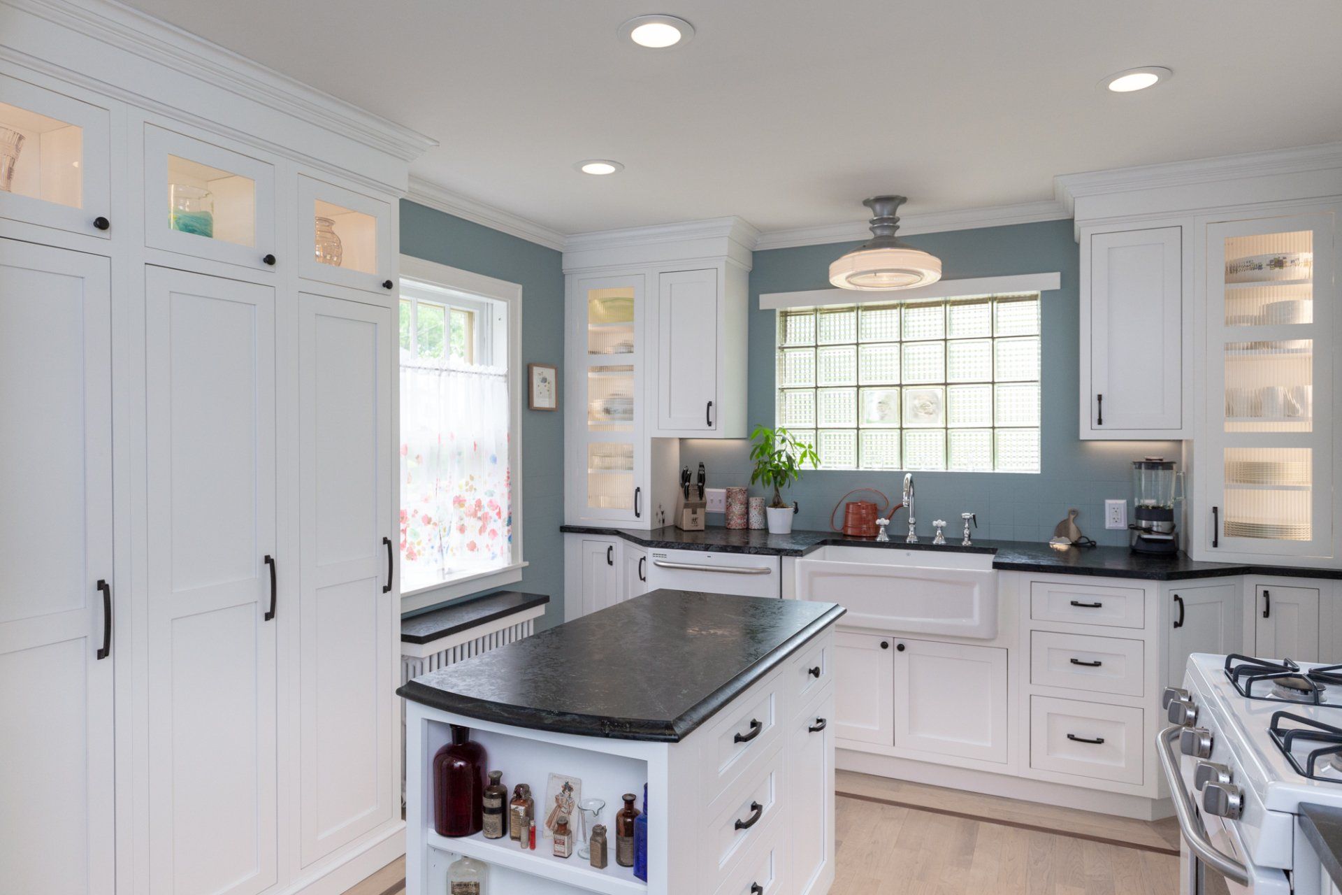 Bright white kitchen with black countertops, central island, window over sink, and gas stove
