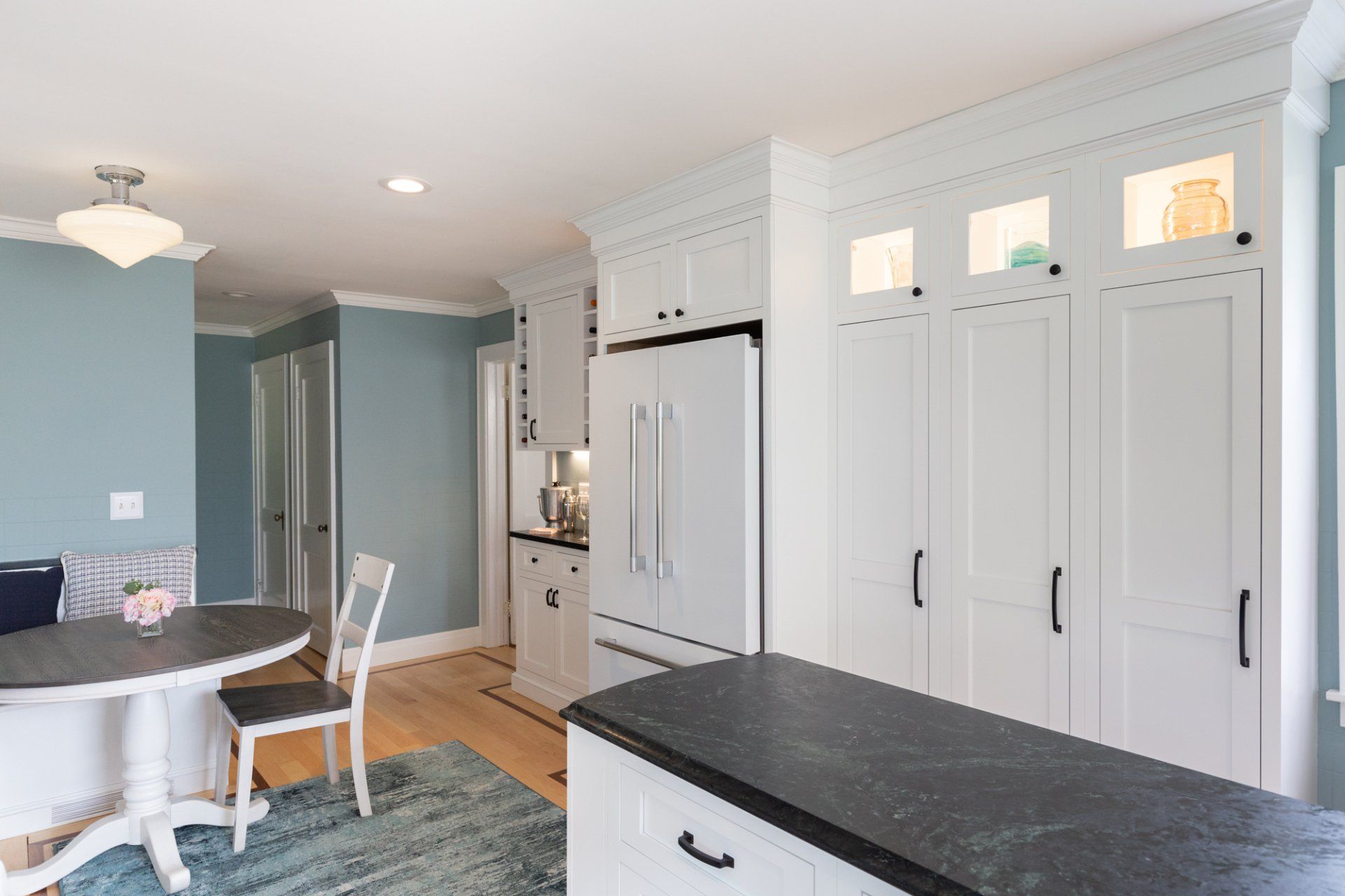 Bright kitchen with white cabinets, black countertops, and a round dining table near a chair