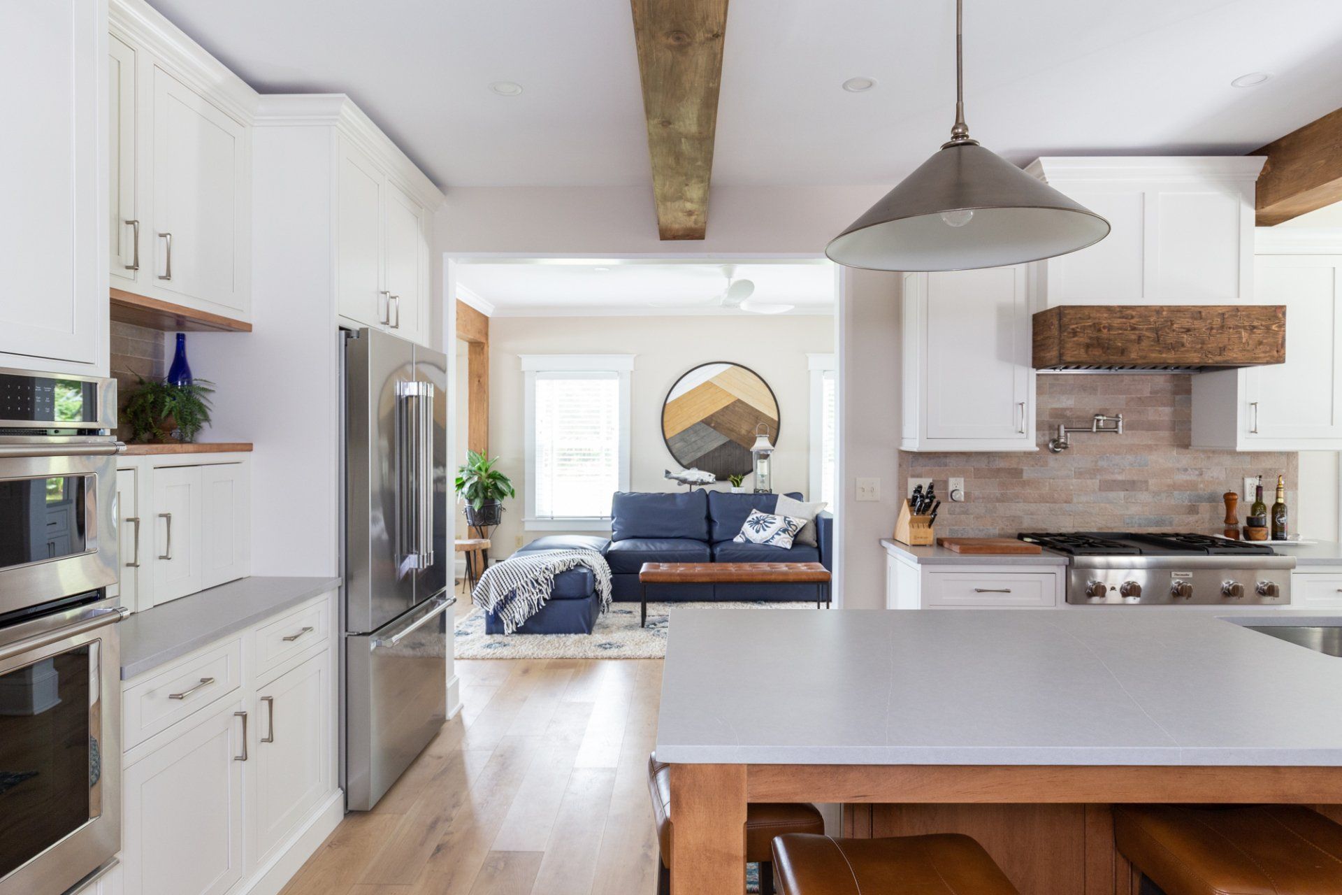 Bright modern kitchen with white cabinets, stainless appliances, and blue sofa in adjacent living room
