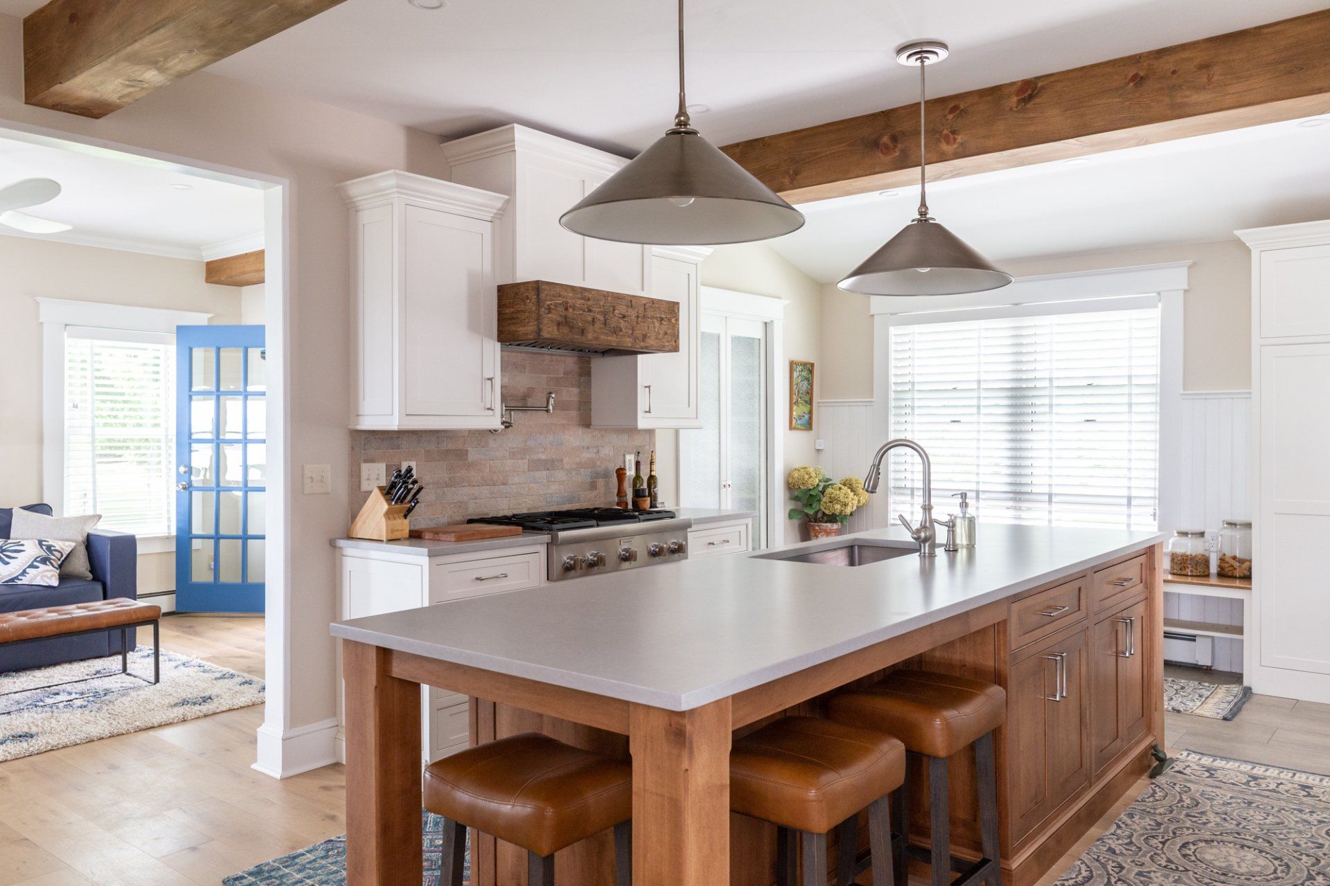 Bright kitchen with island, pendant lights, white cabinets, and wooden stools