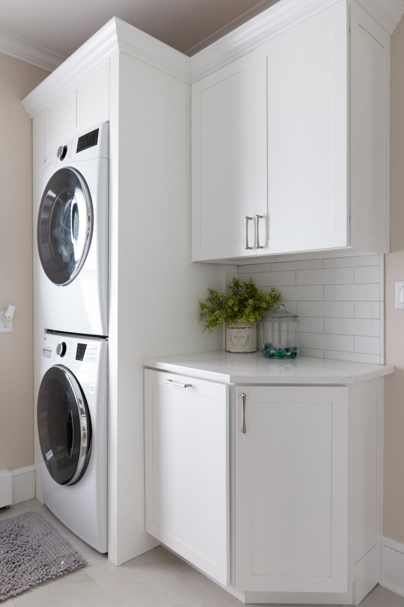 White laundry nook with stacked washer-dryer, cabinets, and a countertop with plants and basket.