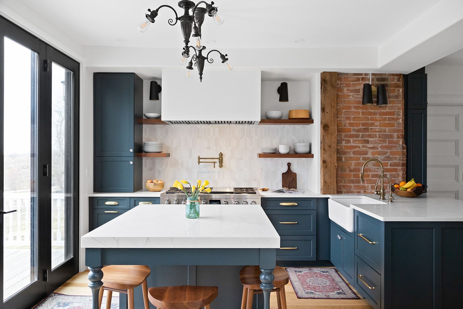 Modern kitchen with navy cabinets, white island, exposed brick wall, and French doors