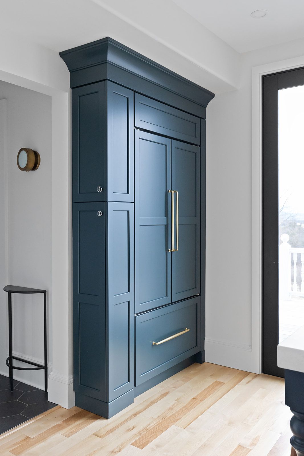 Blue built-in cabinet with brass handles in a bright entryway beside a glass door.