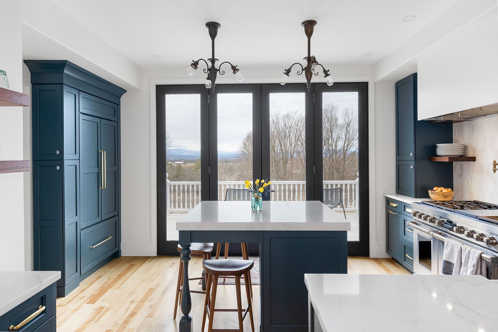 Bright modern kitchen with dark blue cabinets, white island, and large windows overlooking a deck and trees