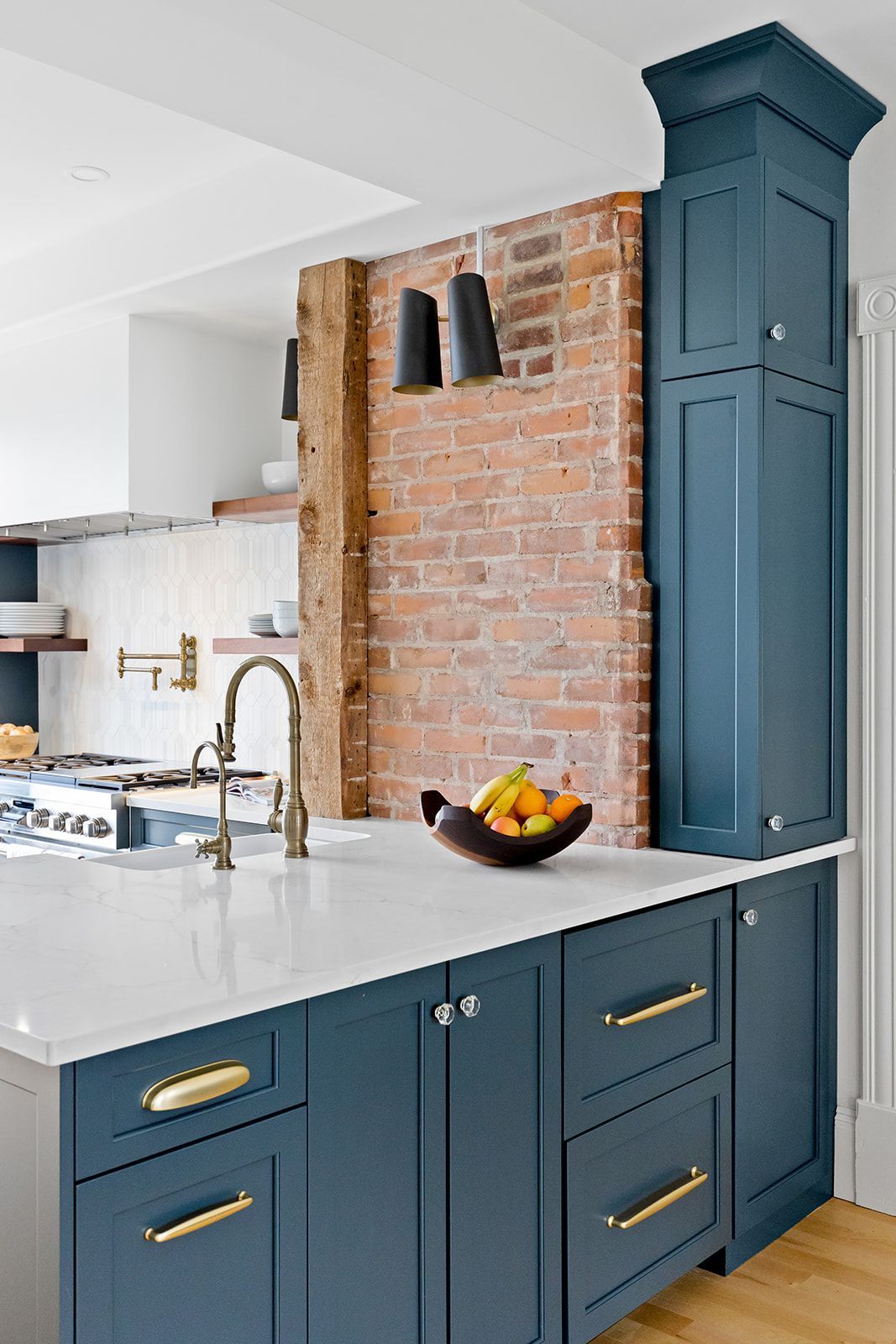 Blue kitchen island with white countertop beside exposed brick wall and tall teal cabinet.