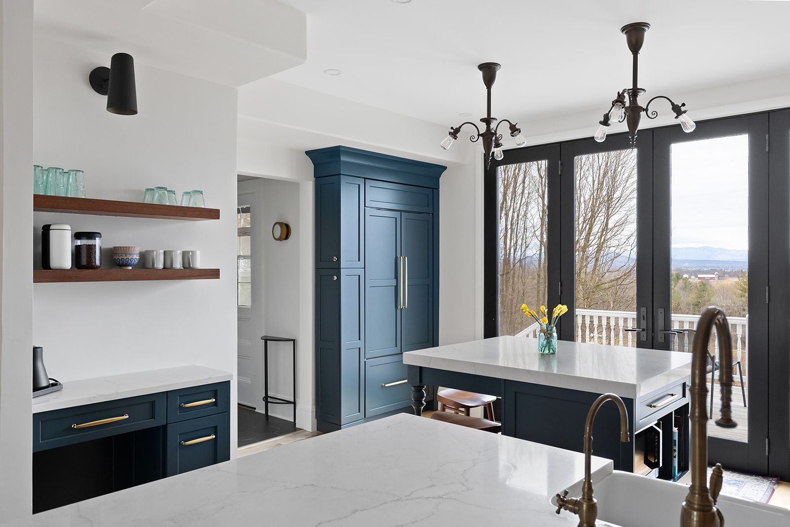 Bright modern kitchen with blue cabinets, white island, and large windows overlooking a landscape