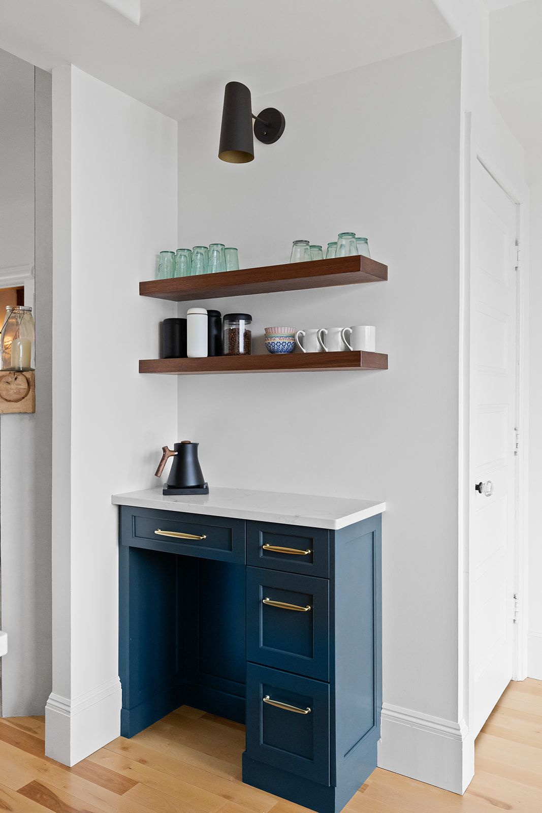 Navy blue built-in desk nook with marble top and floating wood shelves in a white hallway
