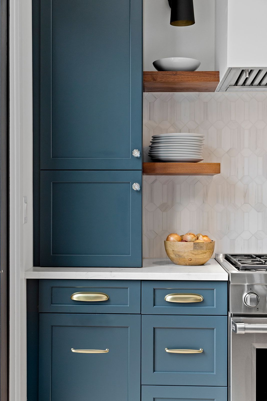 Blue kitchen cabinets with open wooden shelves, stacked dishes, and a stainless stove.