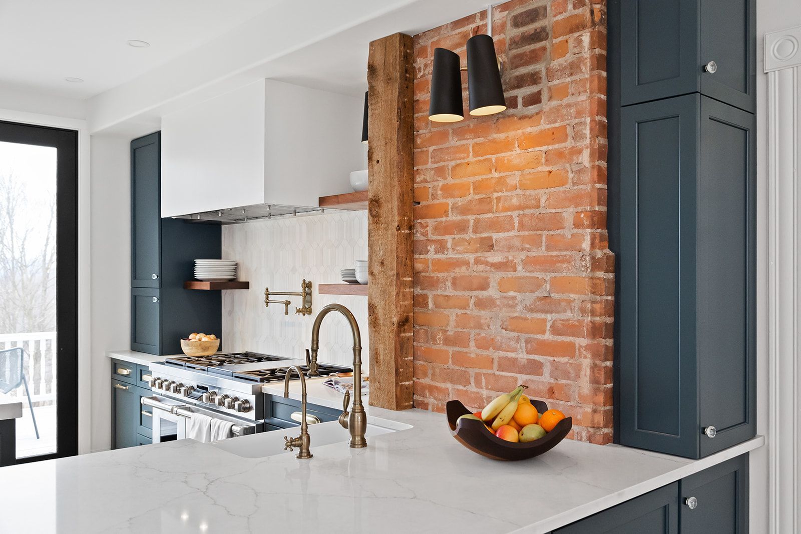 Modern kitchen with brick accent wall, dark cabinets, brass faucet, and fruit bowl on a white island