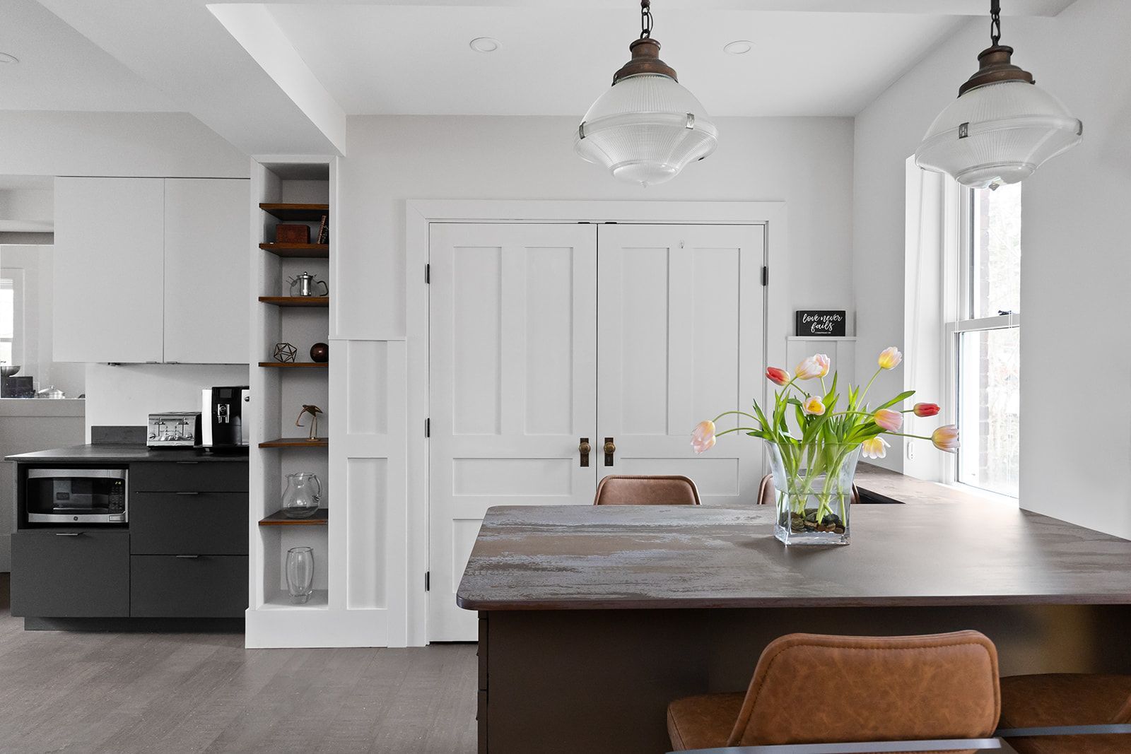 Bright modern kitchen with white cabinets, dark island, pendant lights, and flowers on the counter