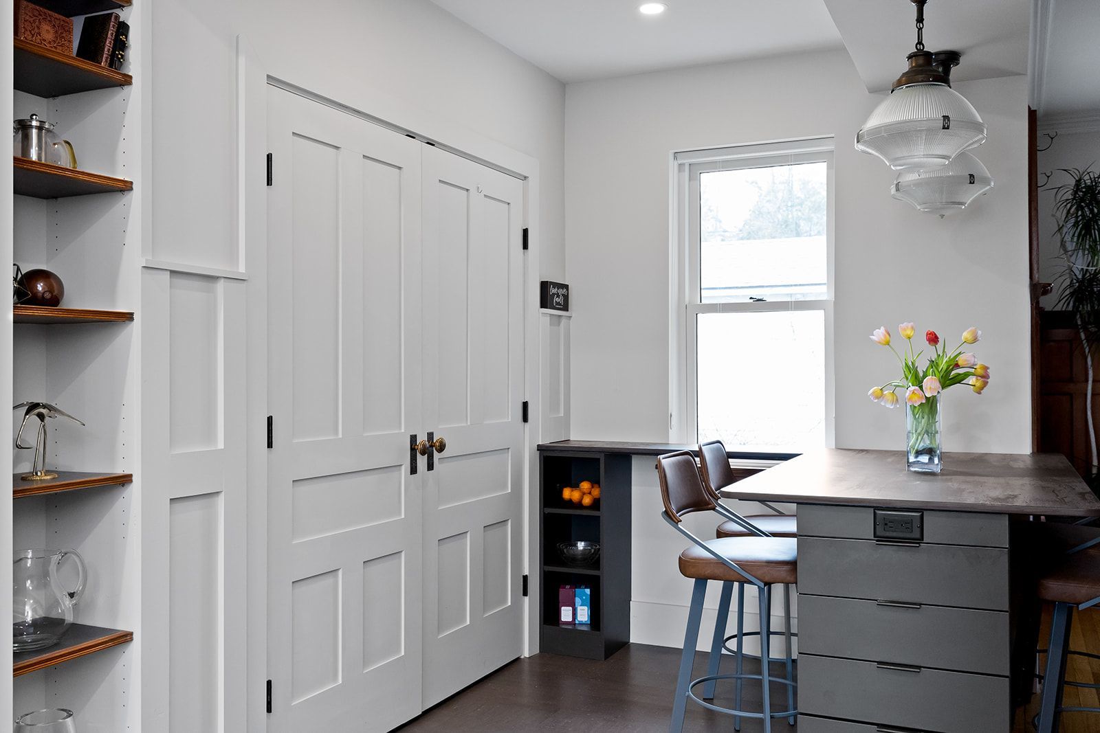 Bright white kitchen nook with double doors, bar stools, a countertop, and flowers by a window
