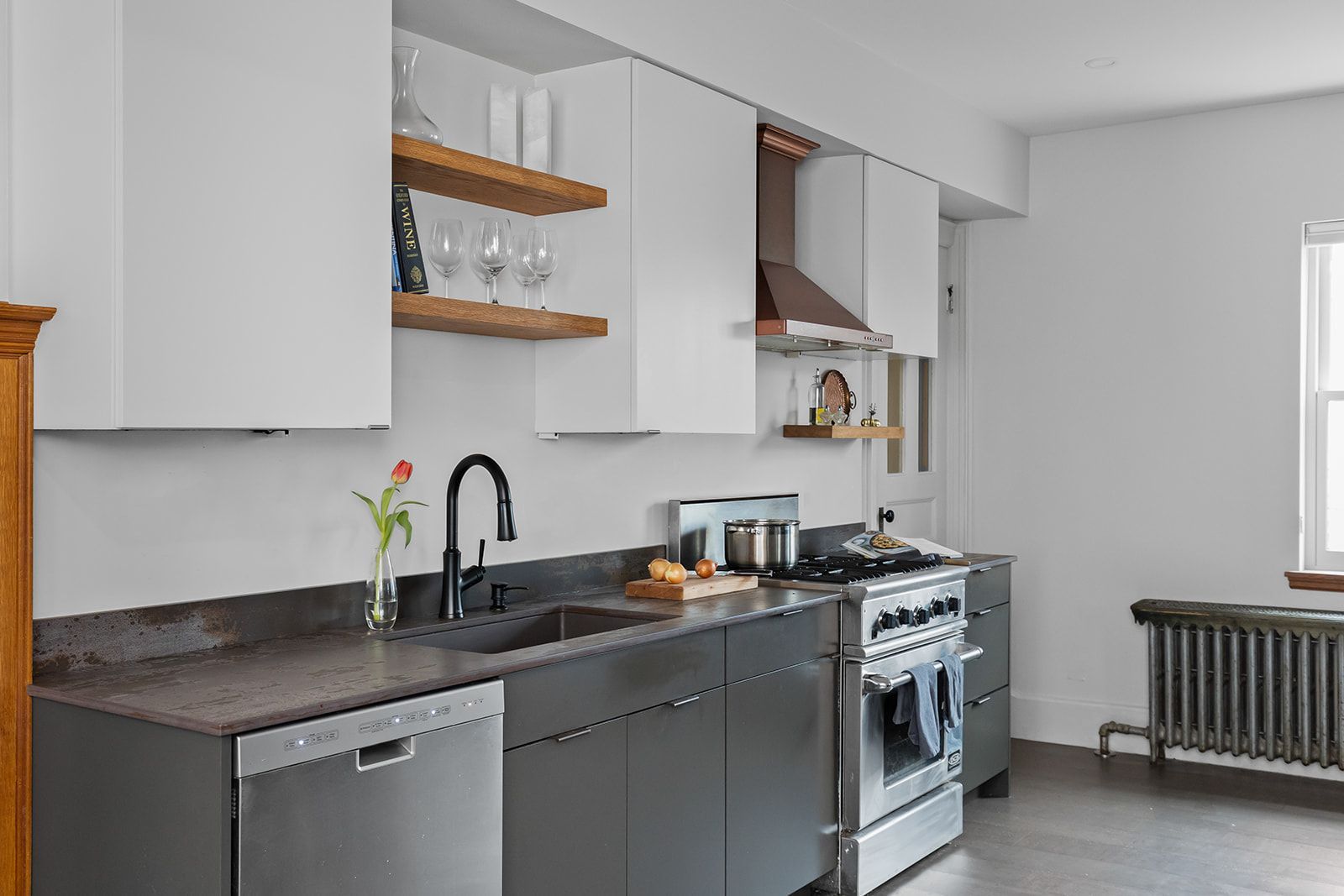 Modern kitchen with white cabinets, dark countertops, stainless stove, and a window radiator