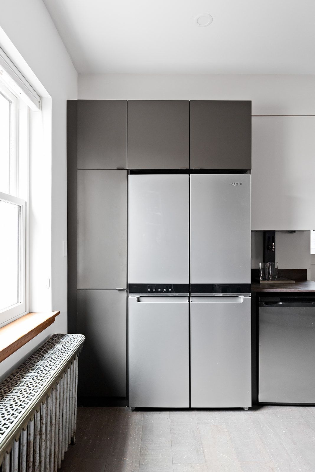 Compact kitchen with stainless steel fridge, dark cabinets, and a window beside a radiator.