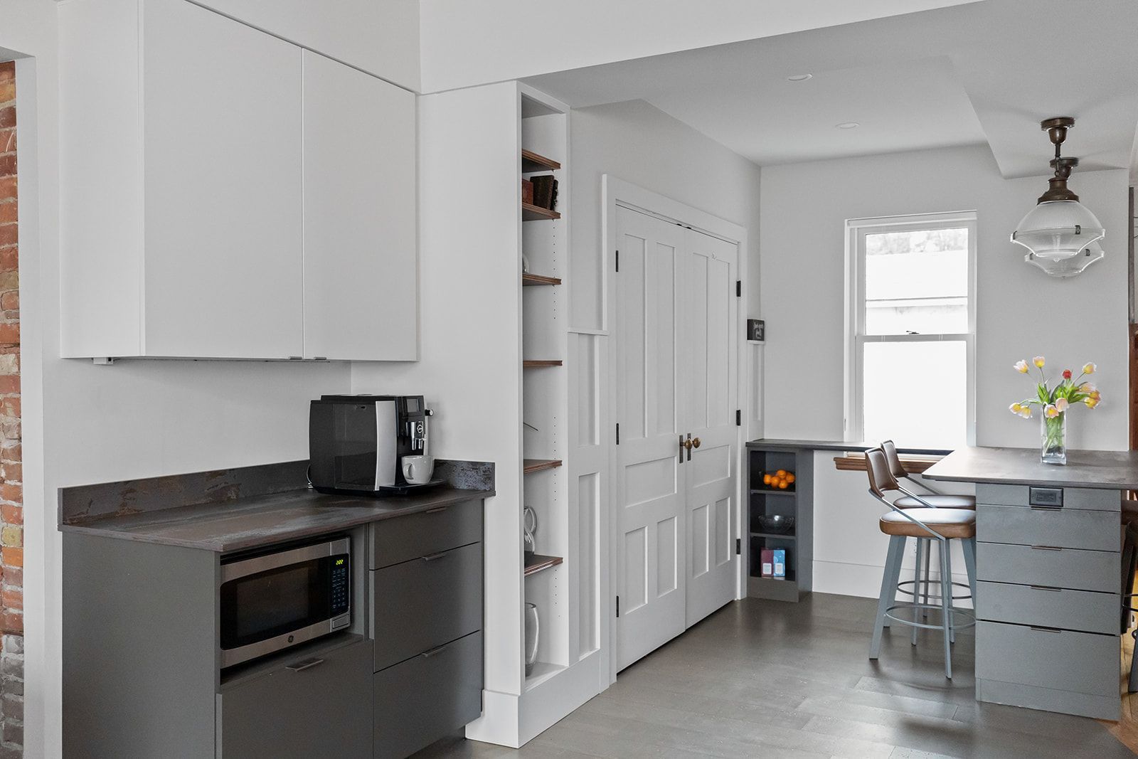 Small modern kitchen with white cabinets, gray island, microwave, and a window-lit dining nook