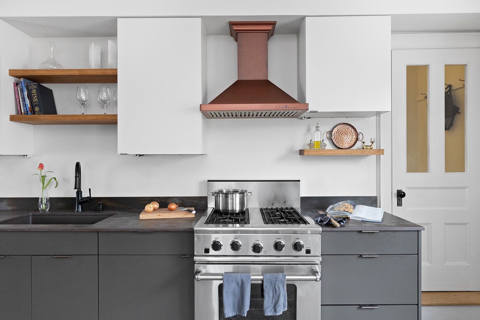 Modern kitchen with white cabinets, dark lower cabinets, copper range hood, and stainless steel stove