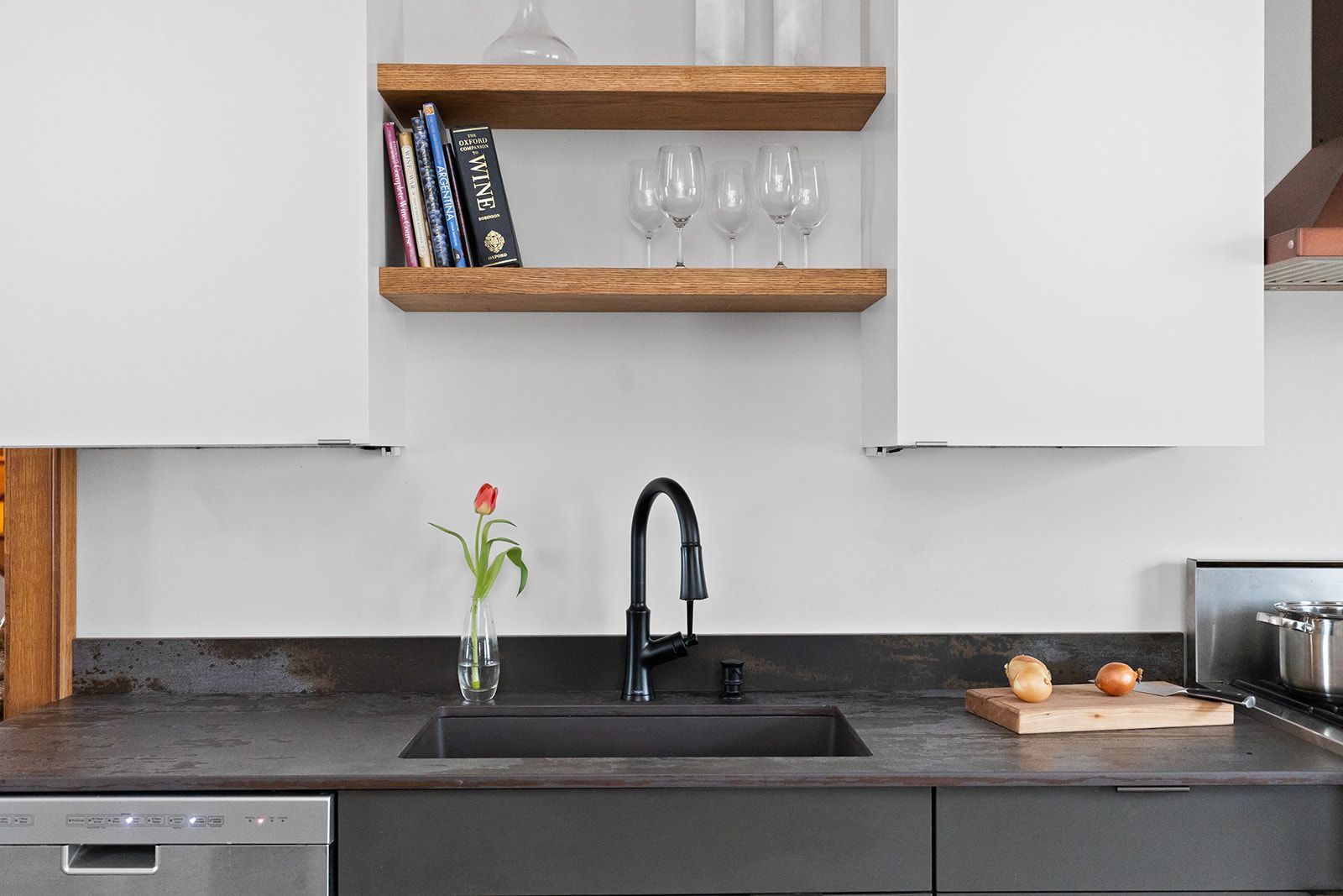 Modern kitchen sink area with black countertop, open wooden shelves, and a vase of flowers