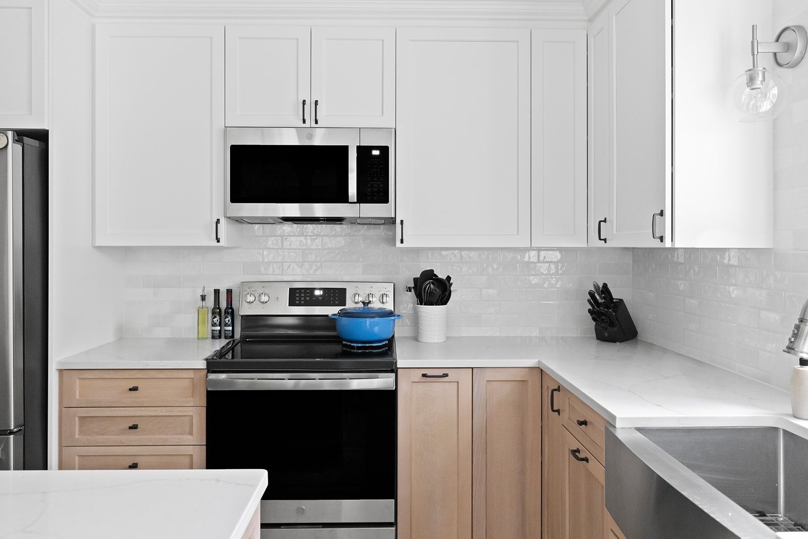 Modern white kitchen with stainless steel appliances, light wood cabinets, and marble-look countertops