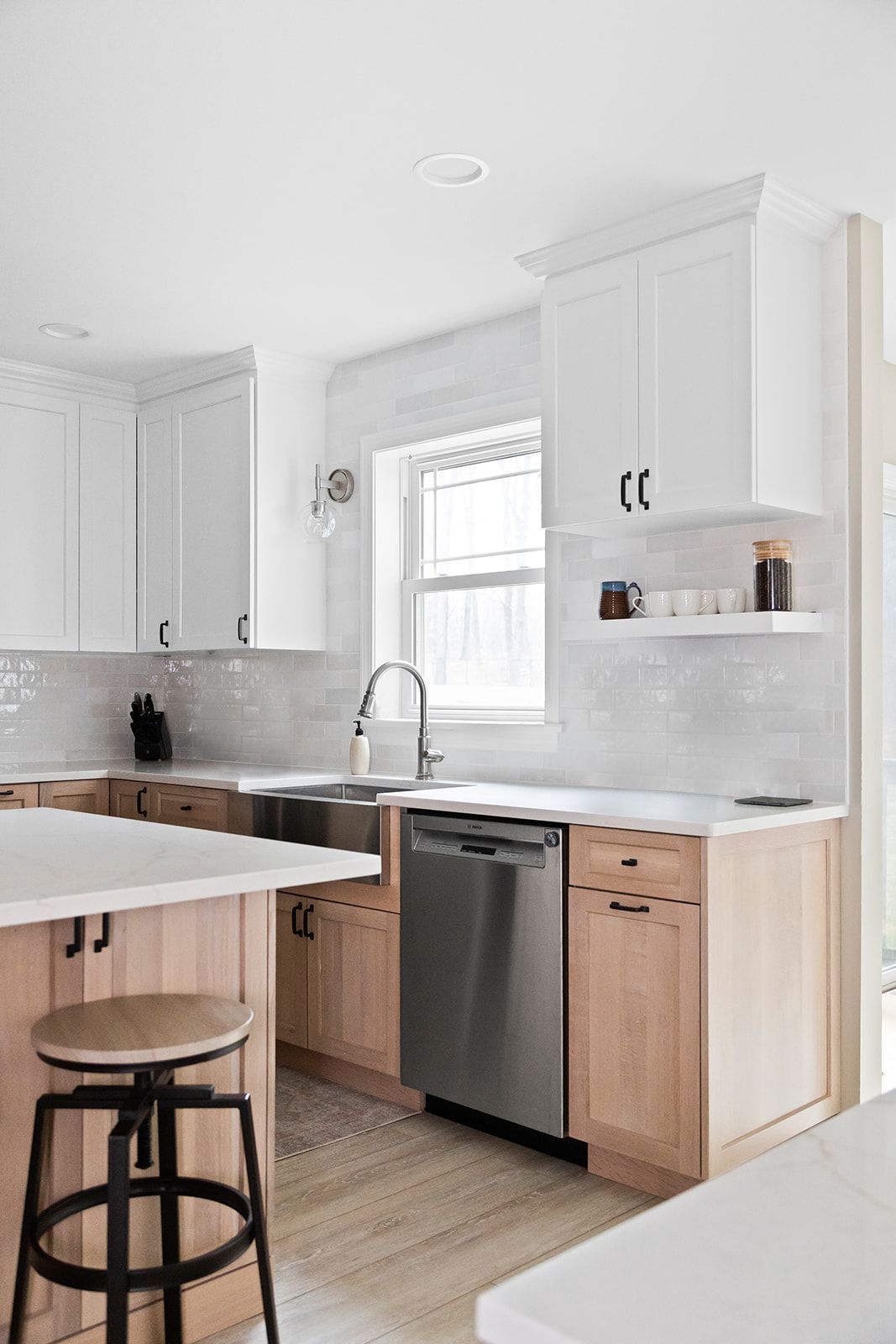 Bright white kitchen with gray cabinets, wood accents, stainless dishwasher, and a stool by the island.