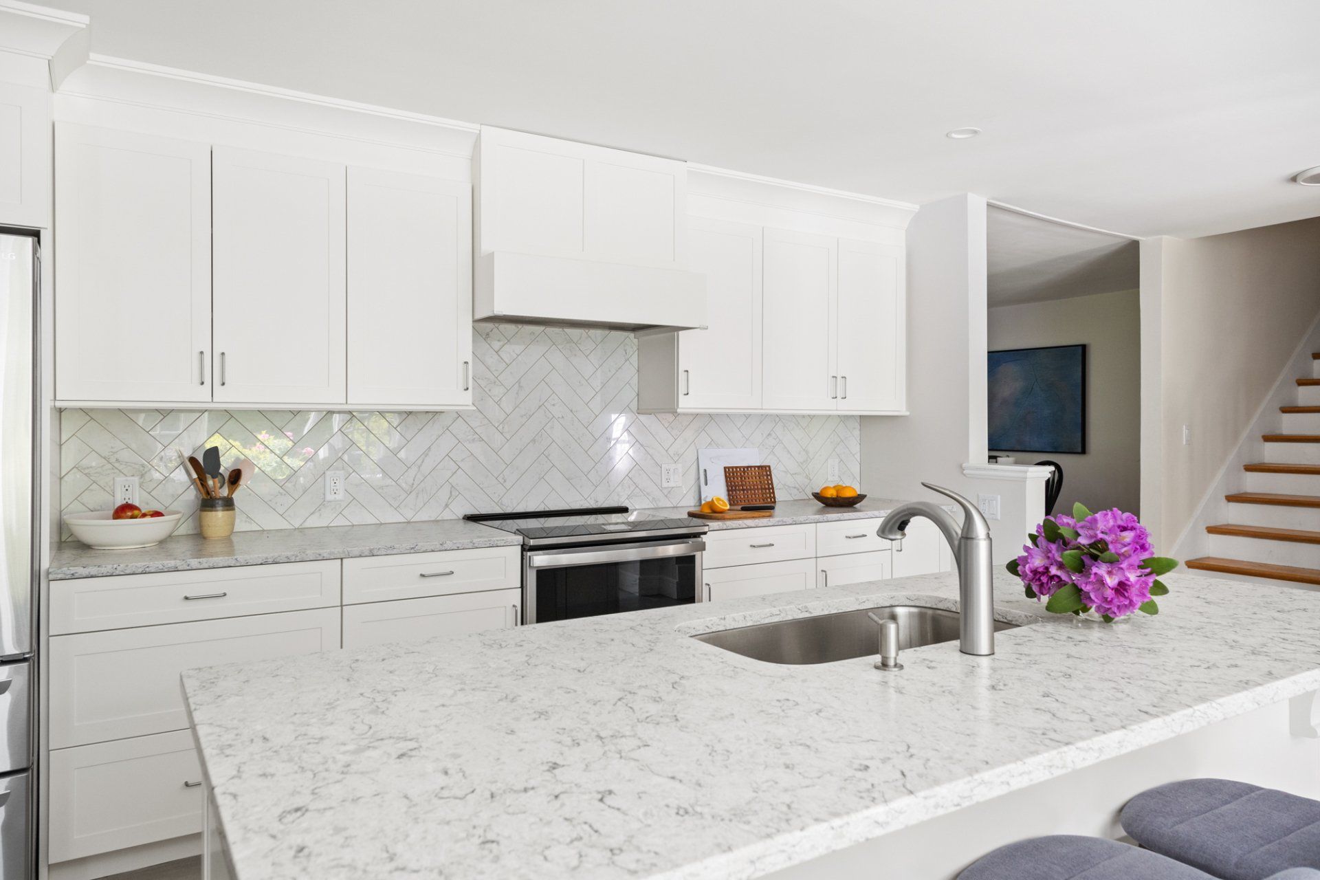 Bright modern kitchen with white cabinets, granite island, stainless appliances, and a flower arrangement