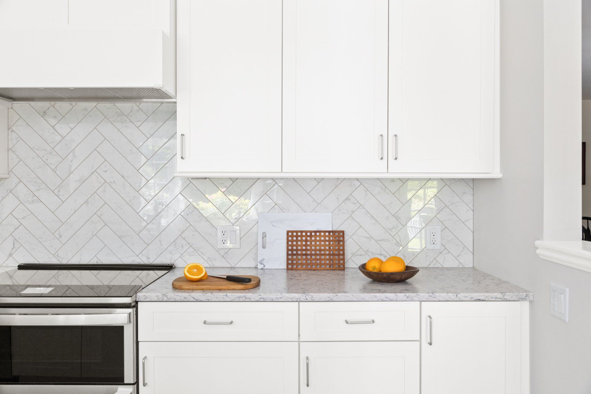 Bright white kitchen with marble backsplash, stainless stove, and fruit on the counter