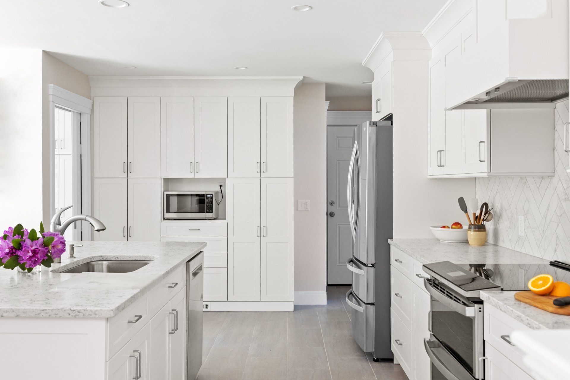 Bright white modern kitchen with island, stainless steel appliances, and purple flowers on the counter
