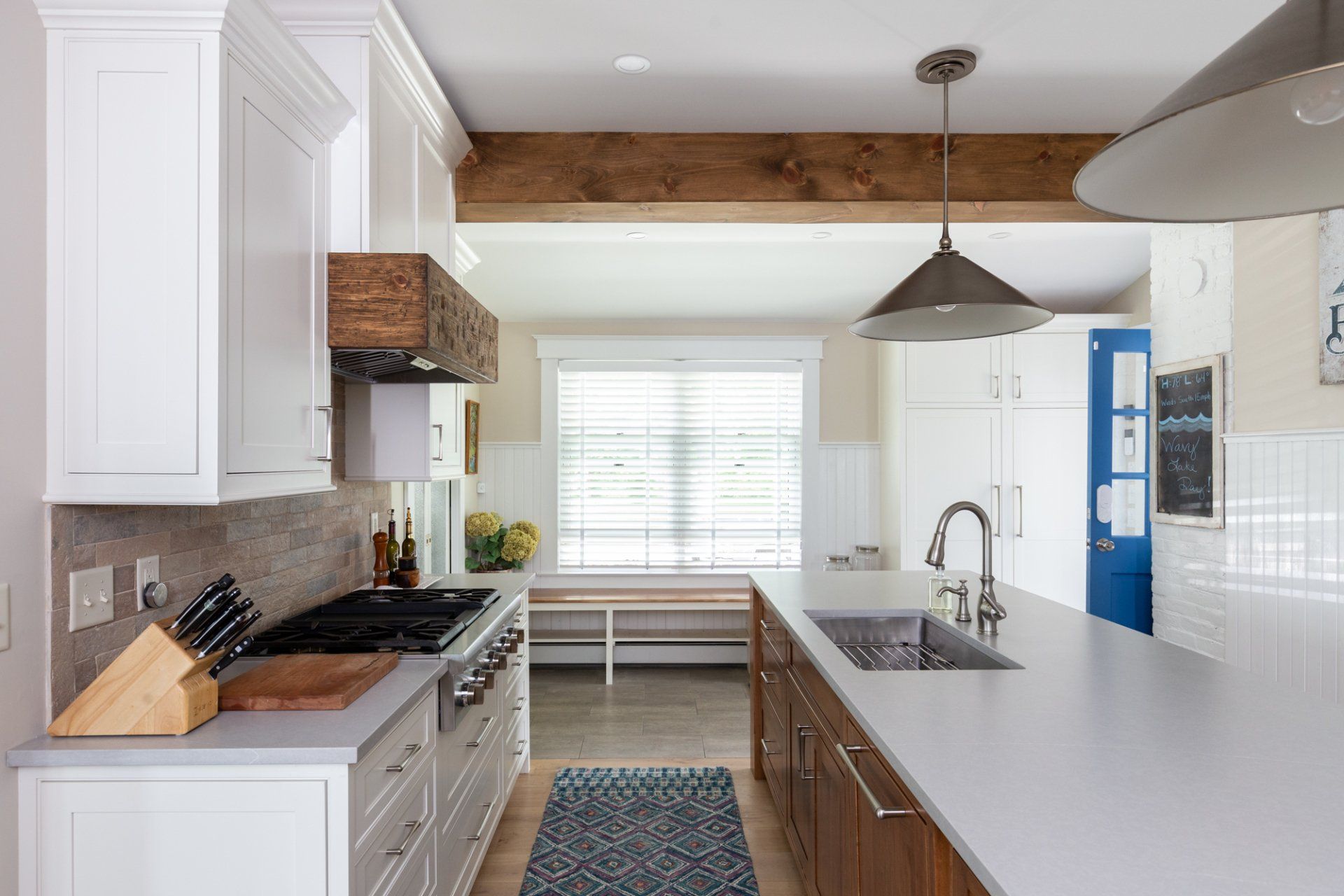 Bright modern kitchen with white cabinets, wood beams, gray island, and stainless steel appliances