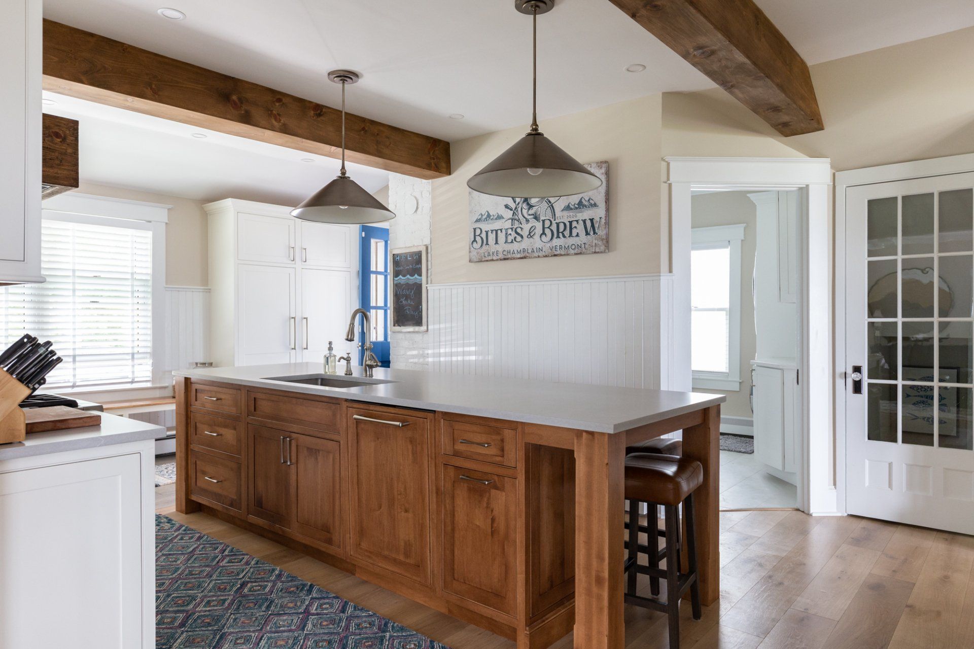 Bright kitchen with a large wooden island, pendant lights, white cabinets, and French doors to the right