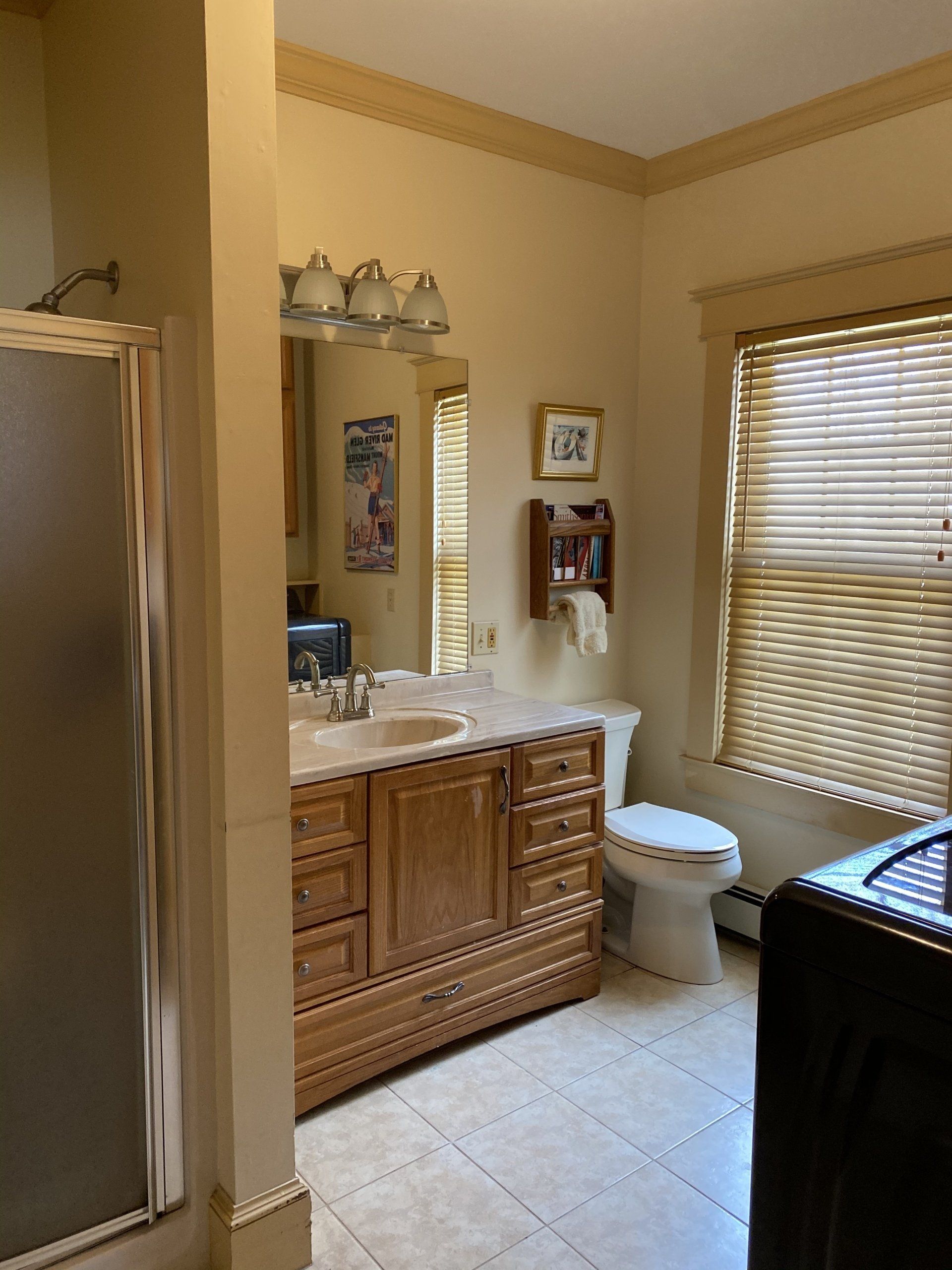 Bathroom with wood vanity, mirror, toilet, and window blinds in beige tones