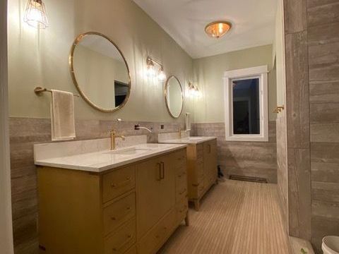 A bathroom with two sinks , two mirrors and a window.