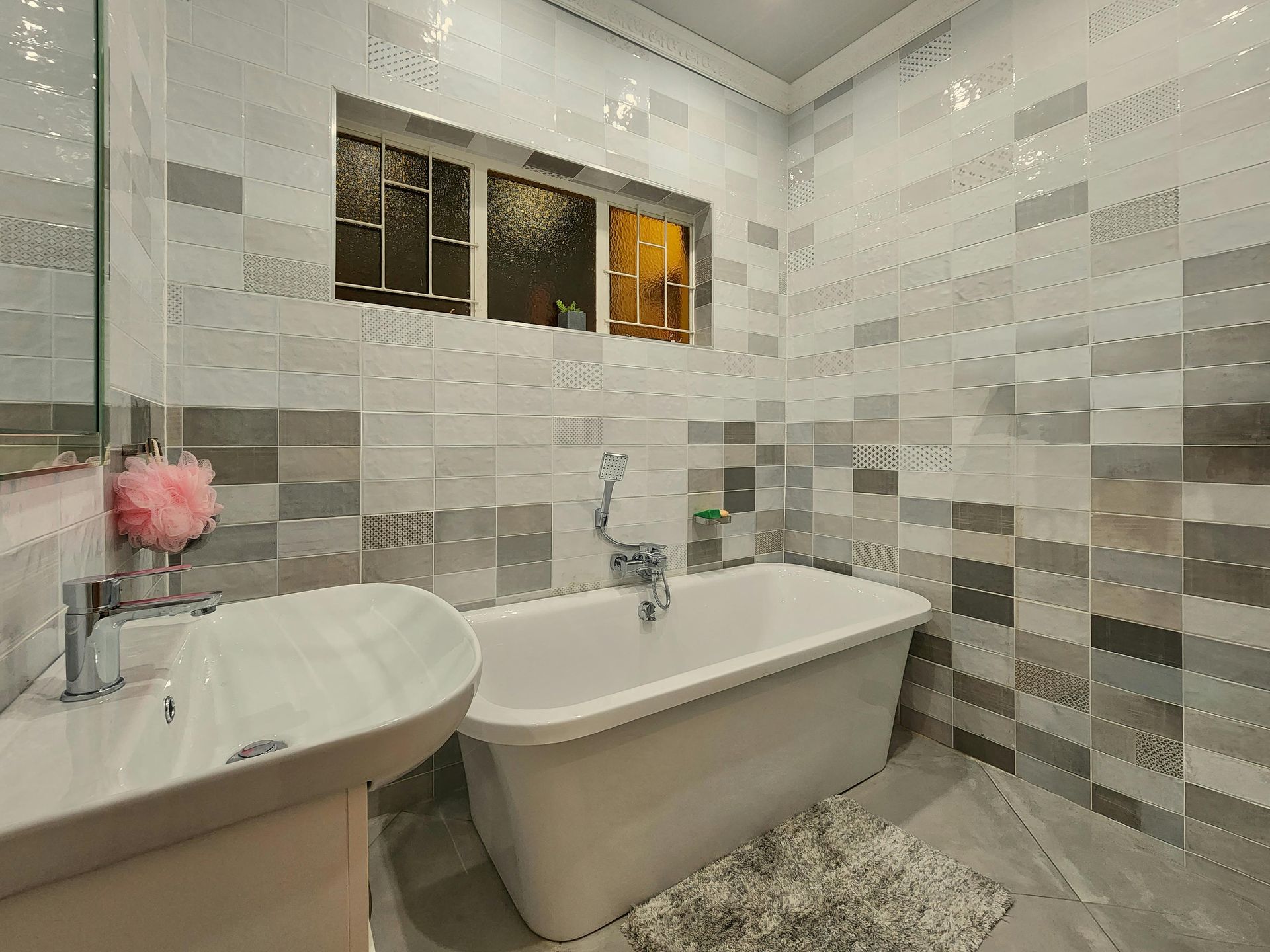 A bathroom with a tub , sink , mirror and window.