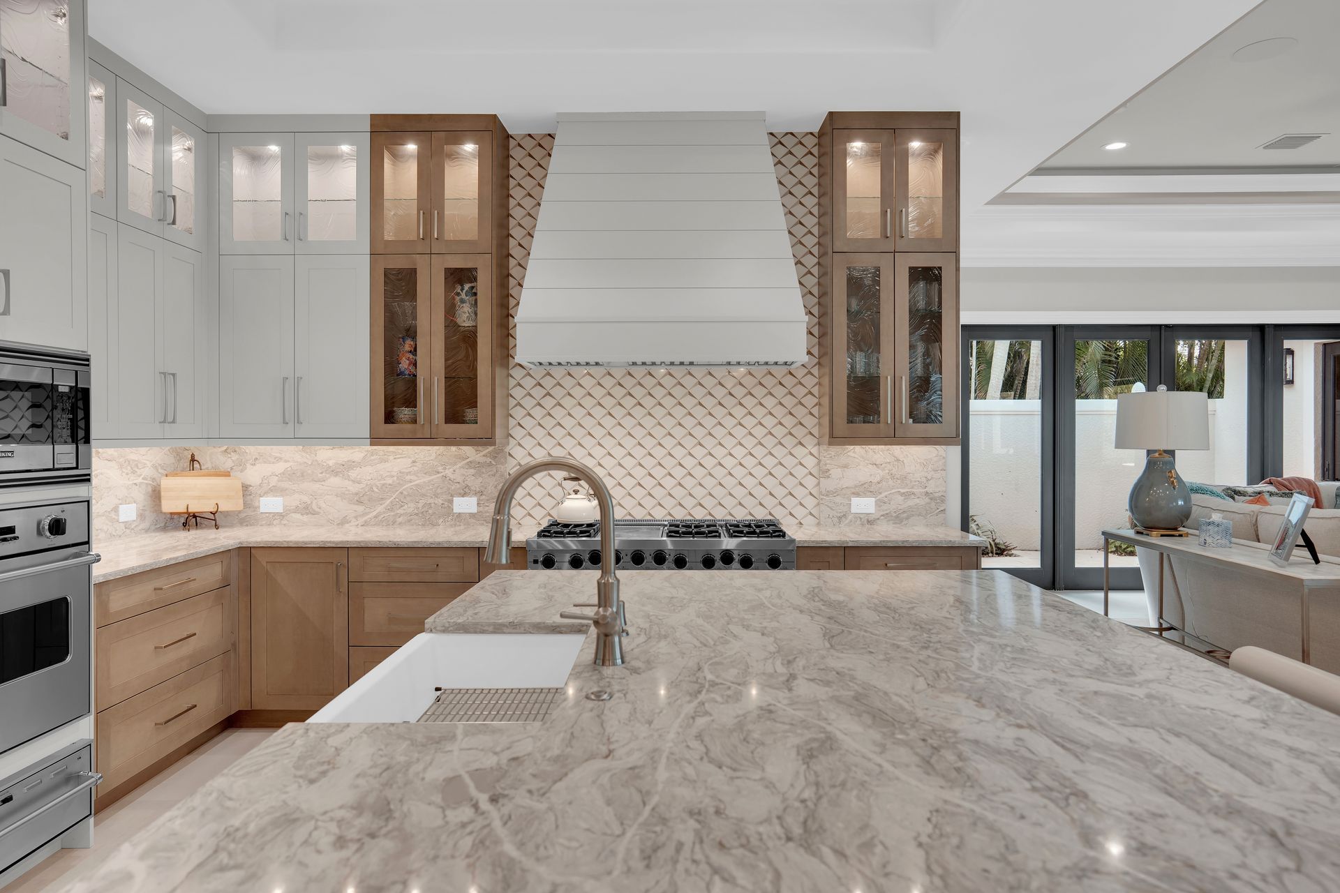 Modern kitchen with island, marble countertops, wood cabinets, and range hood.
