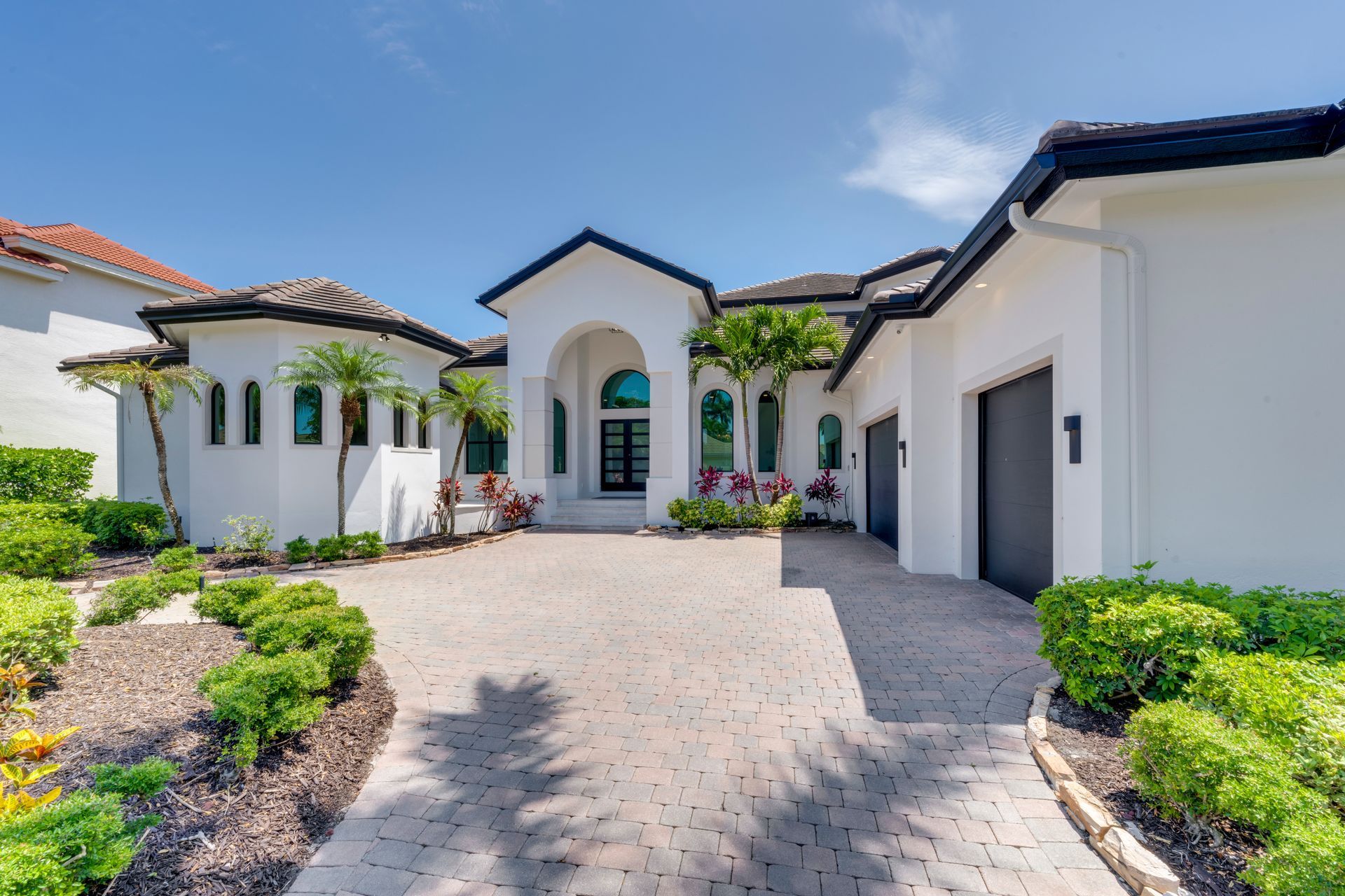 White stucco home with black trim, circular driveway, and green landscaping.