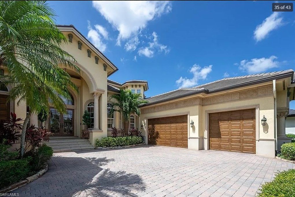 Elegant cream-colored house with a two-car garage, palm trees, and blue sky.