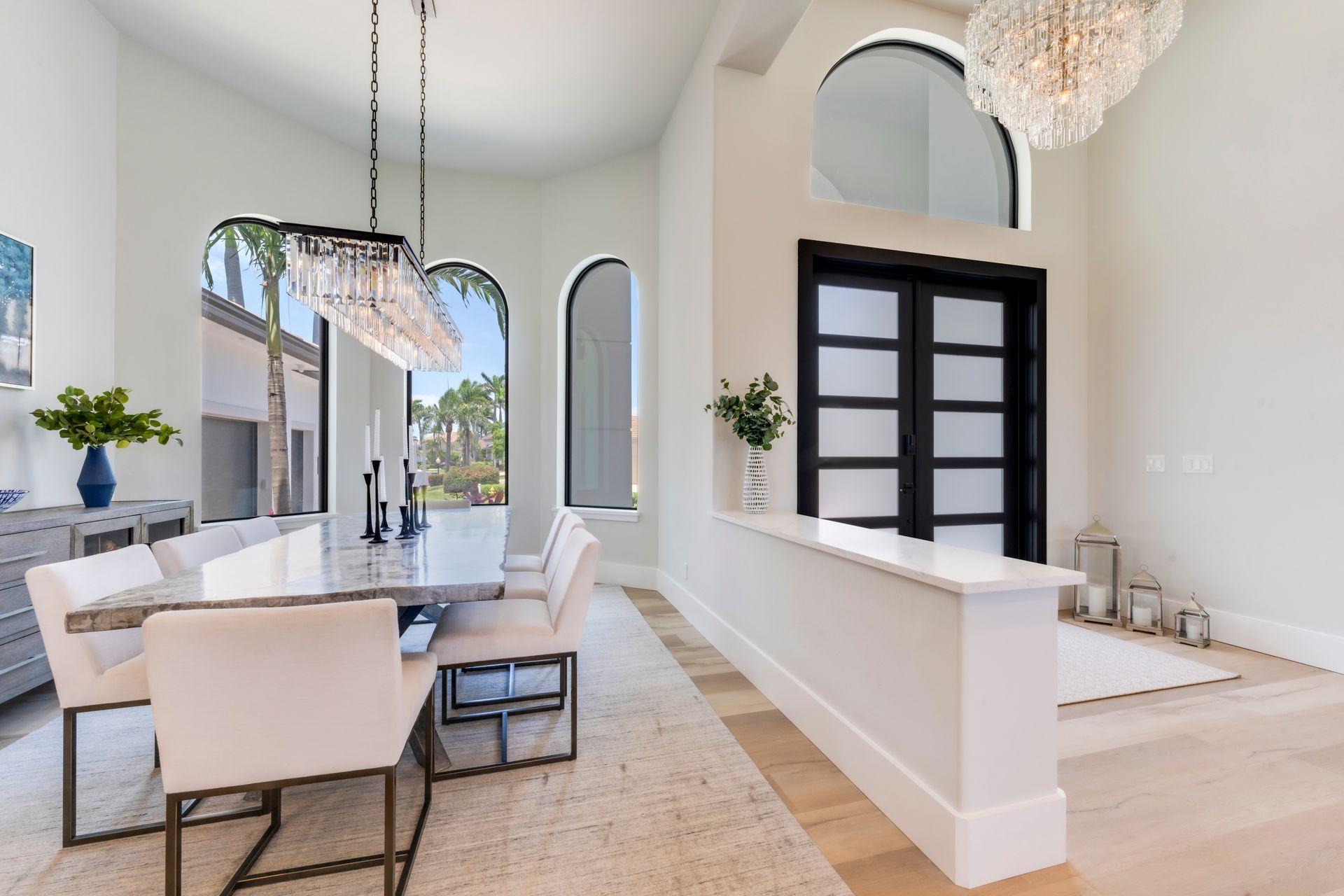 Elegant dining room with arched windows, chandelier, and a marble-topped table set for a meal.